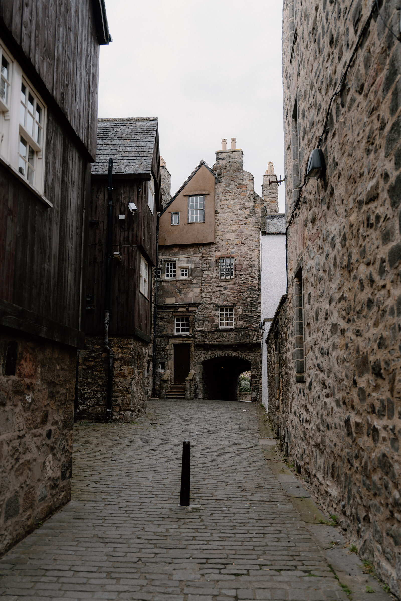 A narrow cobbled close runs between timber-fronted and stone buildings, an archway opening onto the street beyond.