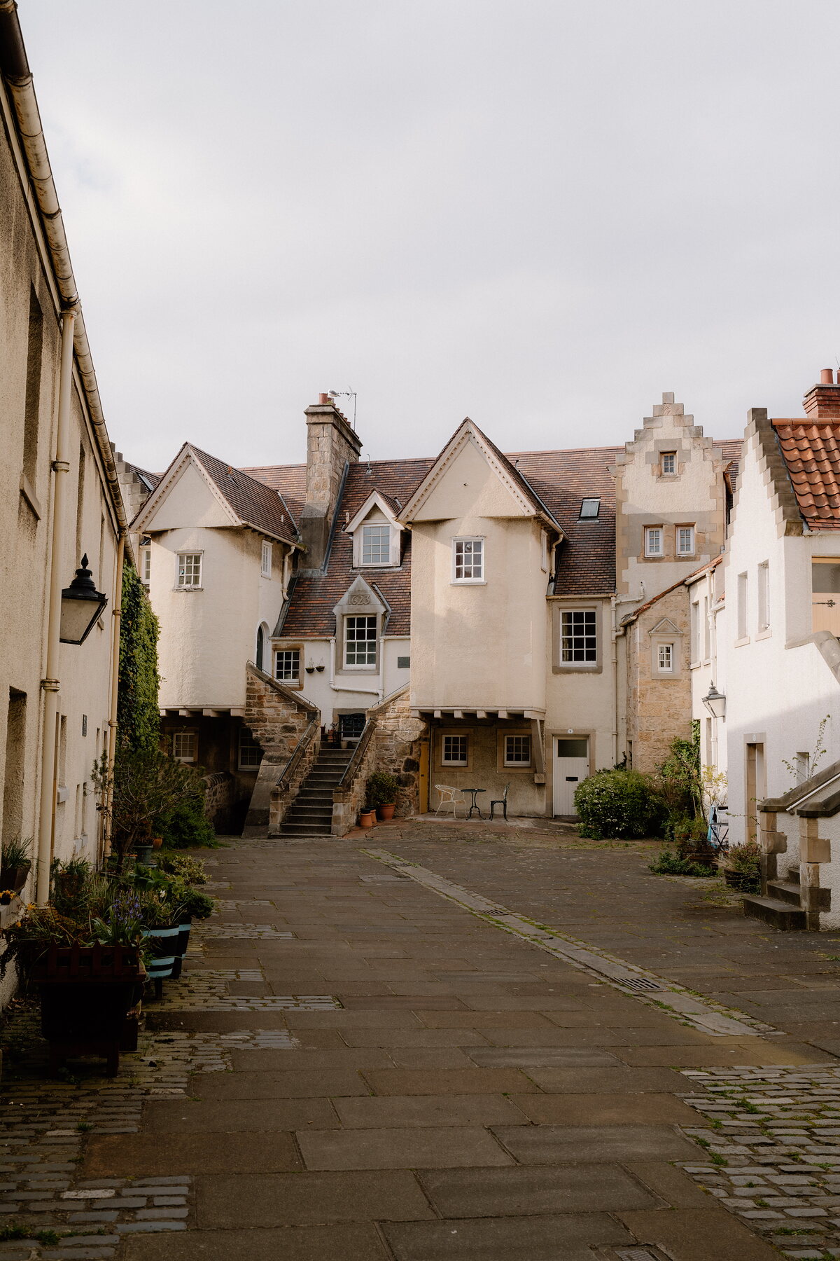 A cobbled courtyard leads to a cluster of harled Scots-Baronial houses with turrets, crow-stepped gables and outdoor stone stairs.