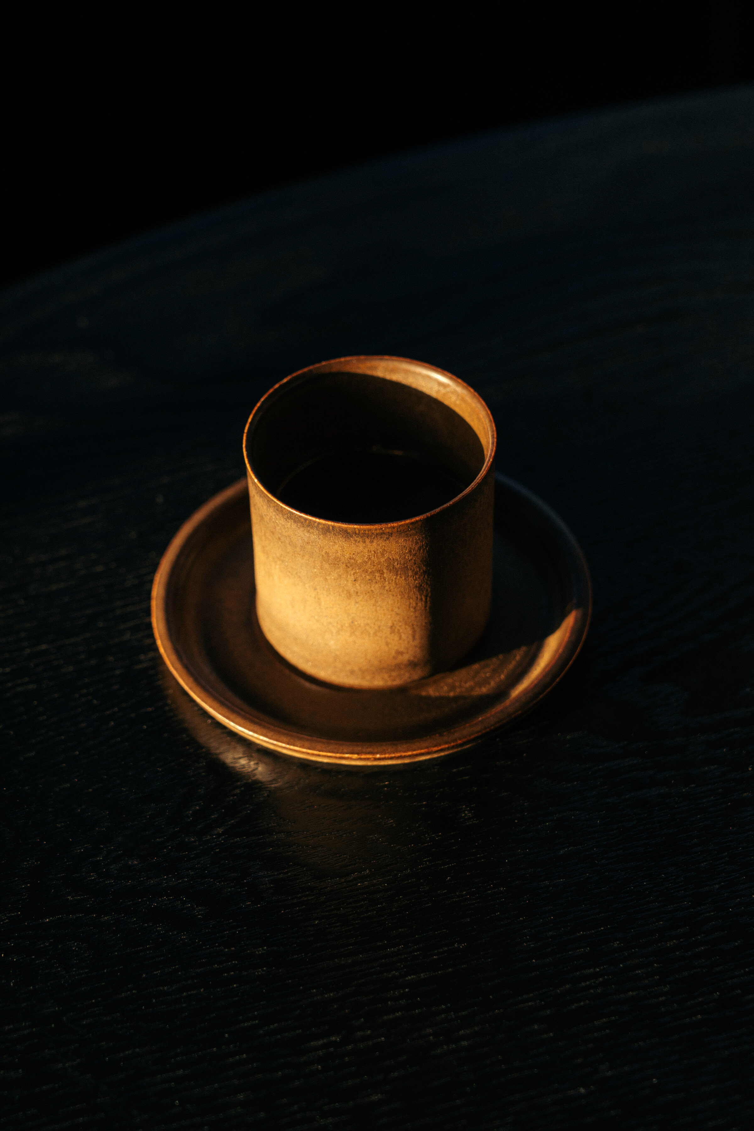 A cup of onion broth on its saucer, lit warm against a black table.