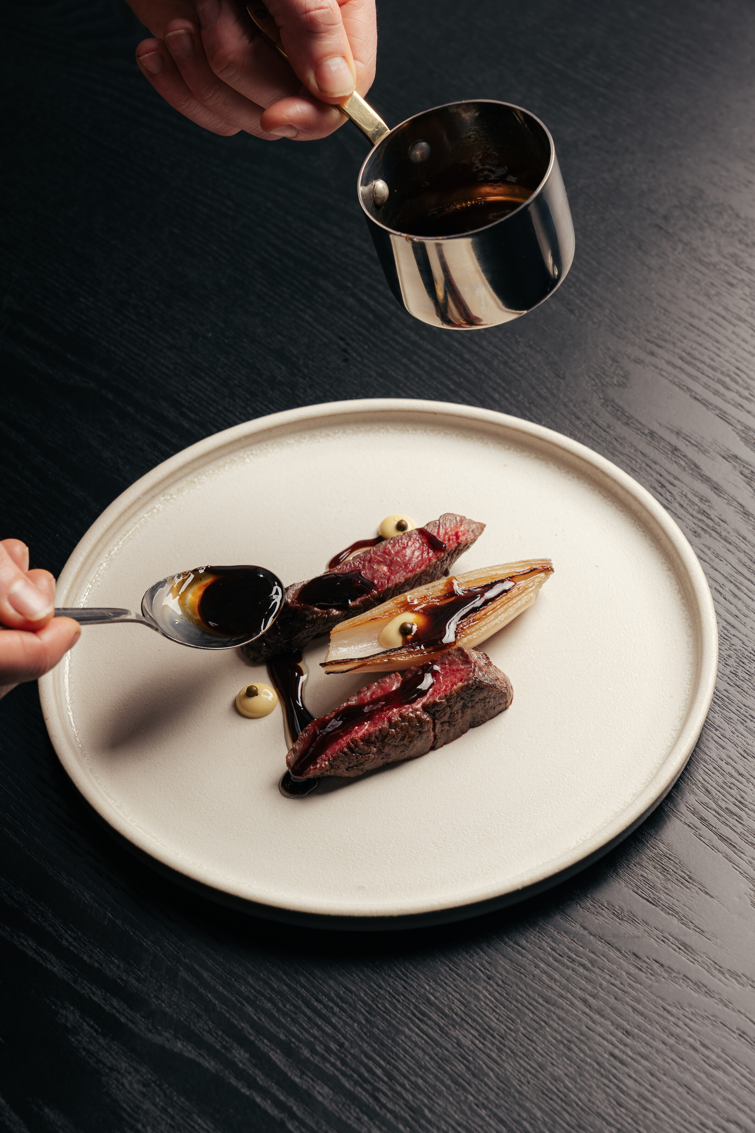Sauce being spooned over slices of Free Co sirloin with peppercorns and tallow on a white plate.
