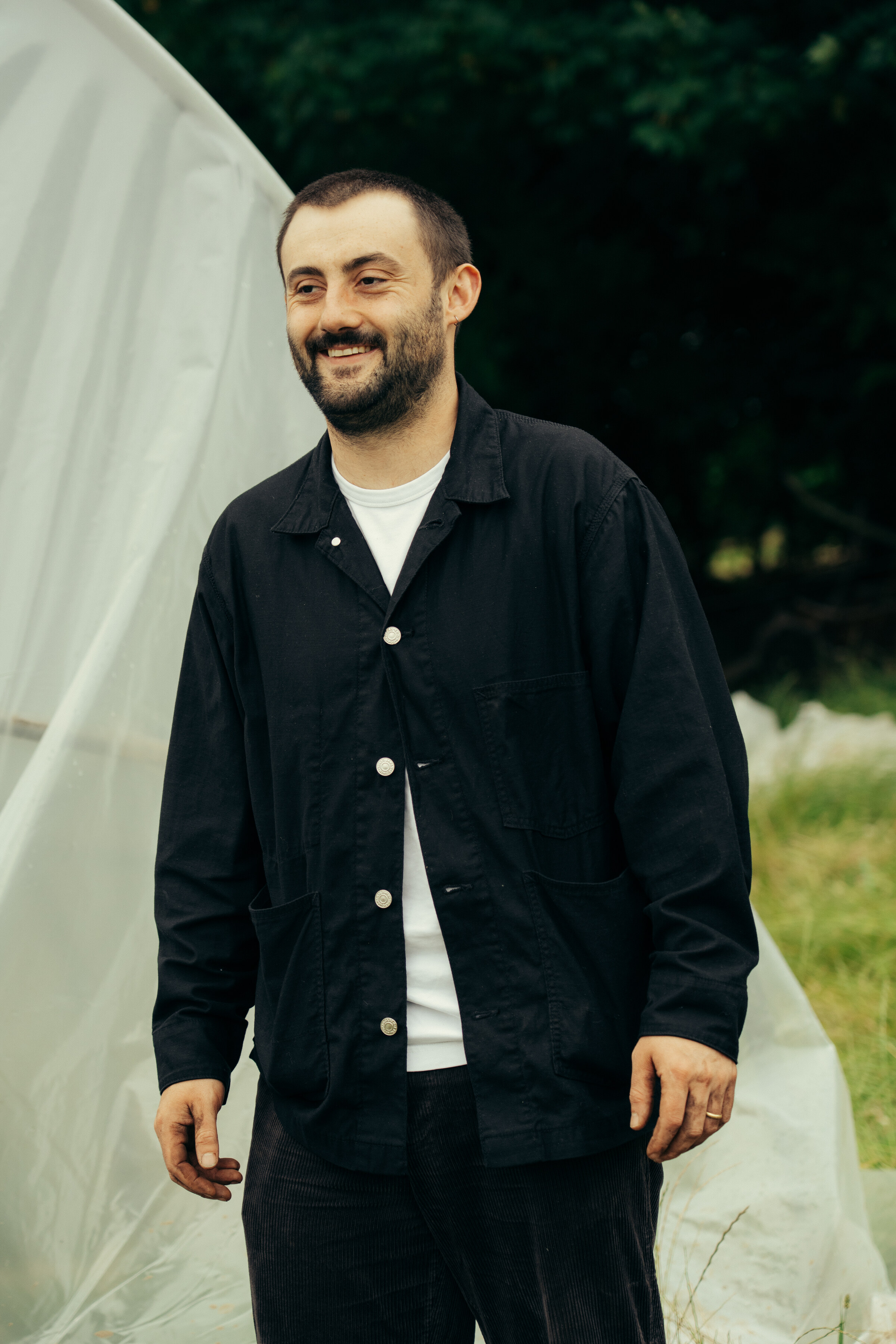 Tomás Gormley smiling in a dark jacket at the kitchen garden, a polytunnel behind him.