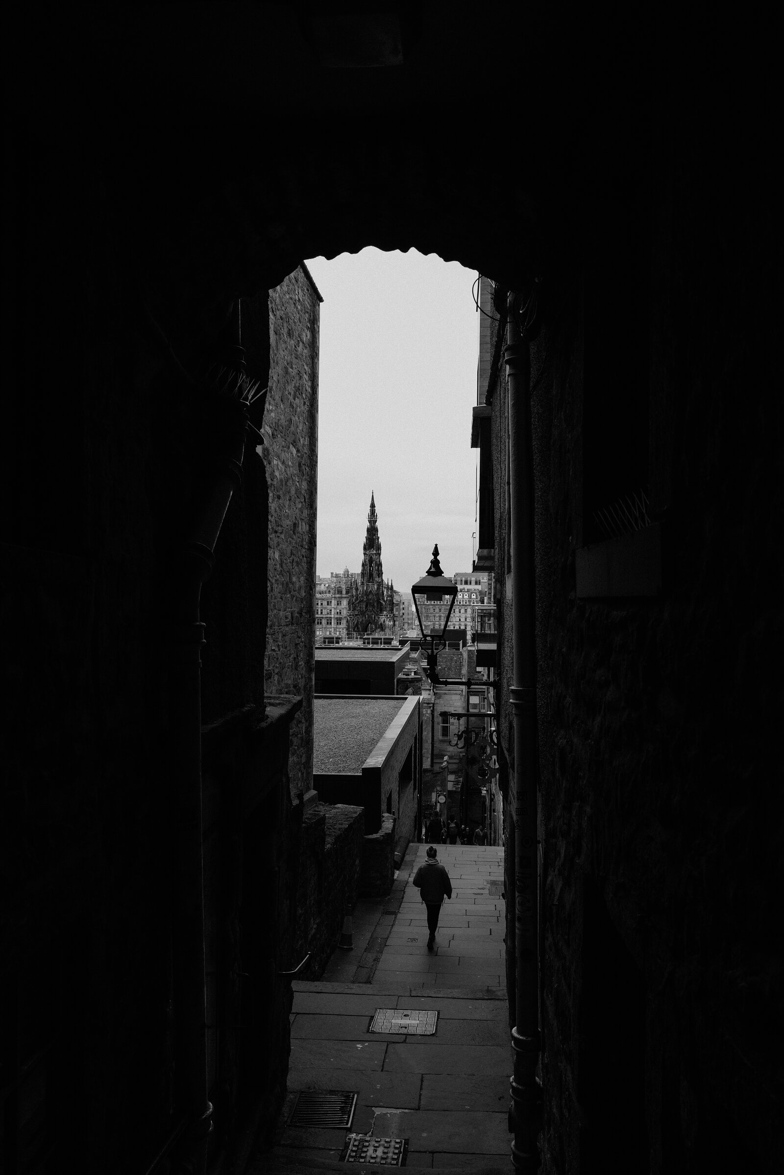 A figure walking down a stone close towards the Scott Monument, shown in black and white