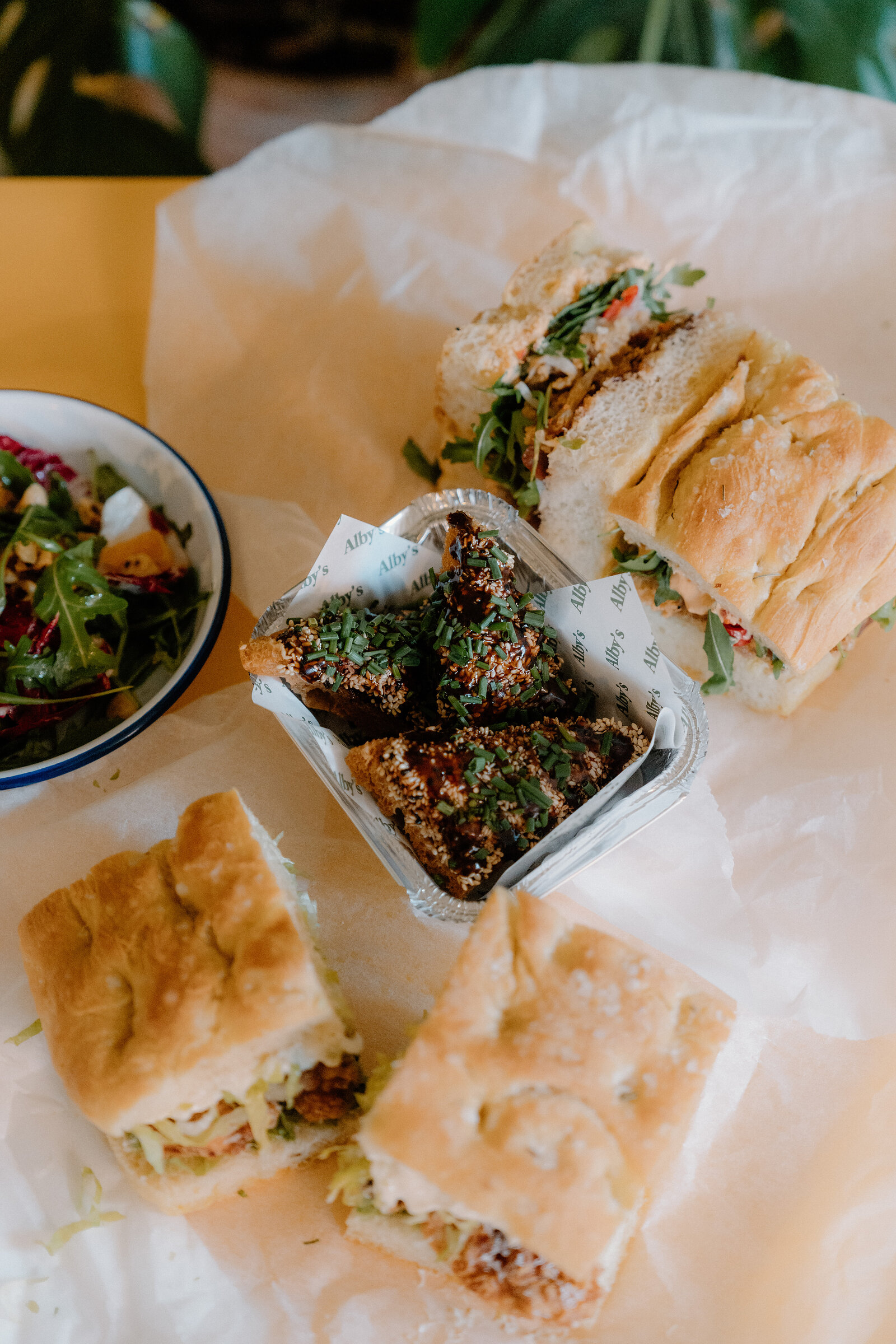 Sandwiches wrapped in Alby's paper sit beside a bowl of salad on a table.