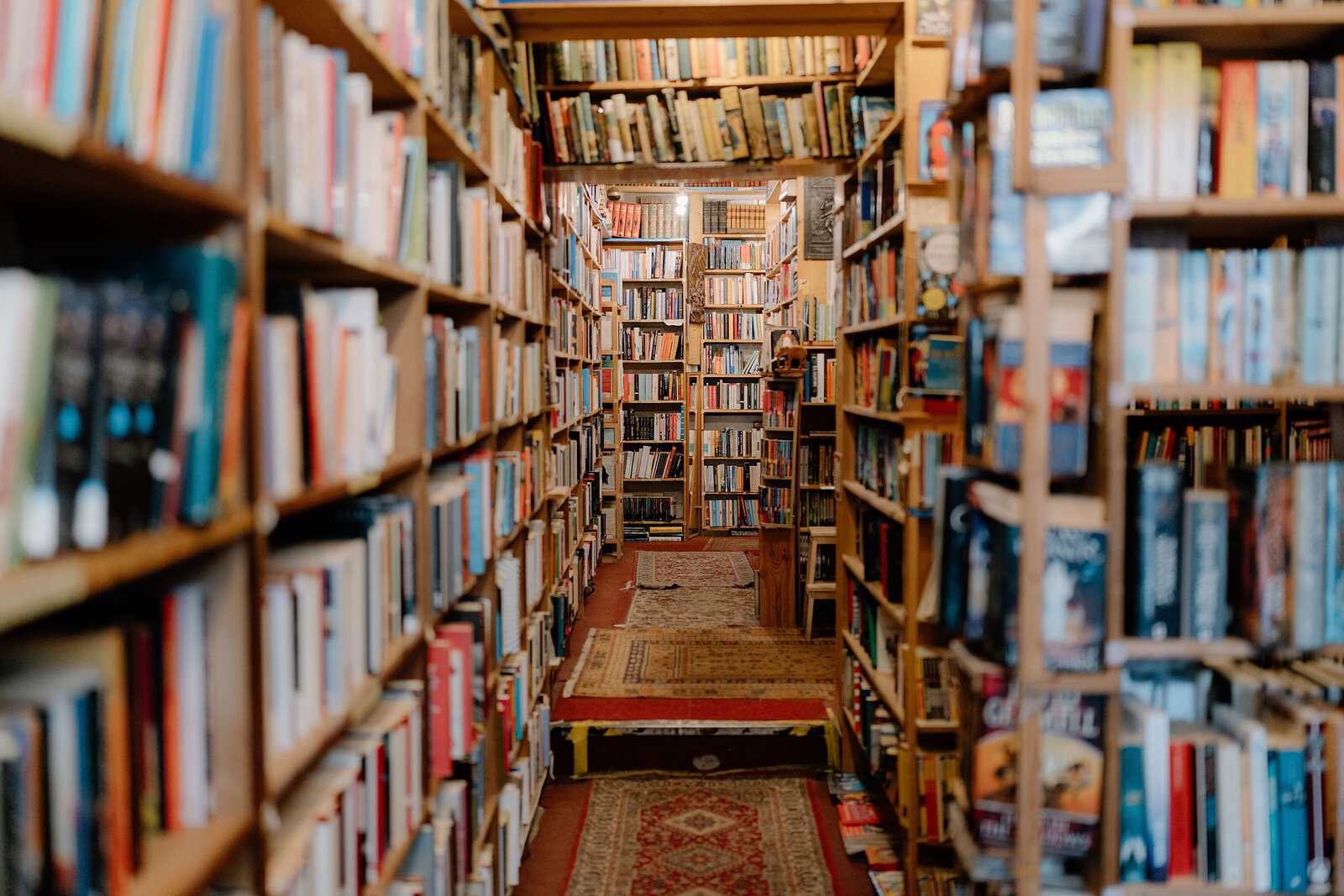 Crowded bookshelves line a narrow aisle laid with patterned rugs.