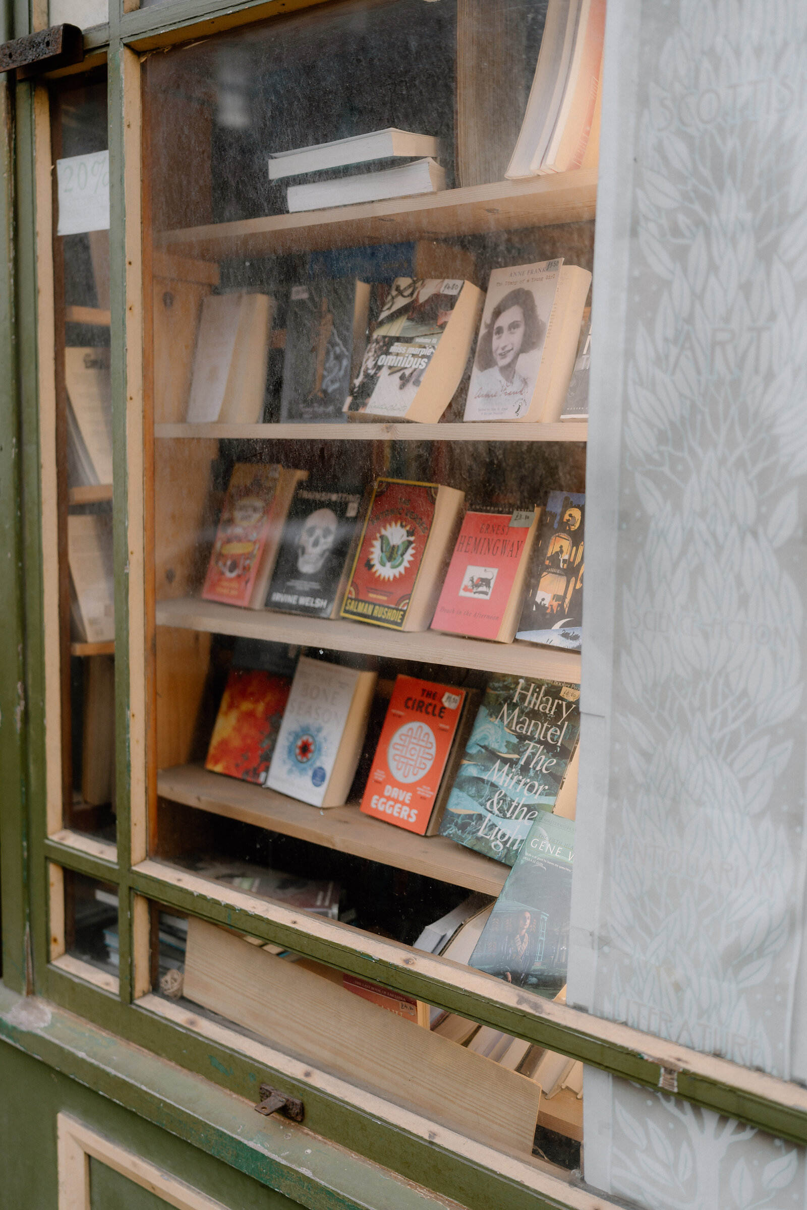 Modern paperback novels line a bookshop's glass display shelves.