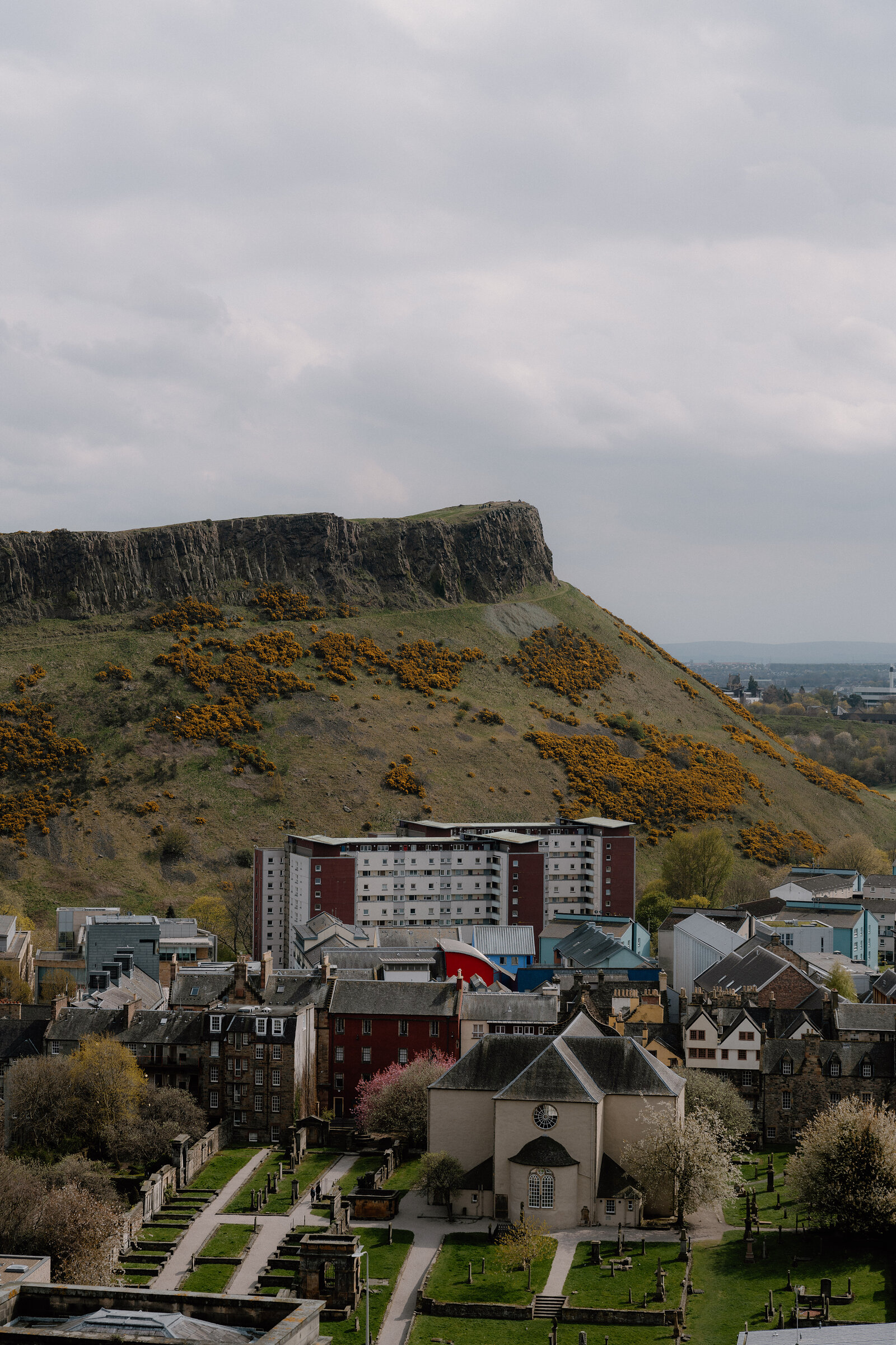 Arthur's Seat and Salisbury Crags rising above a church and graveyard, tower blocks at the foot of the slope