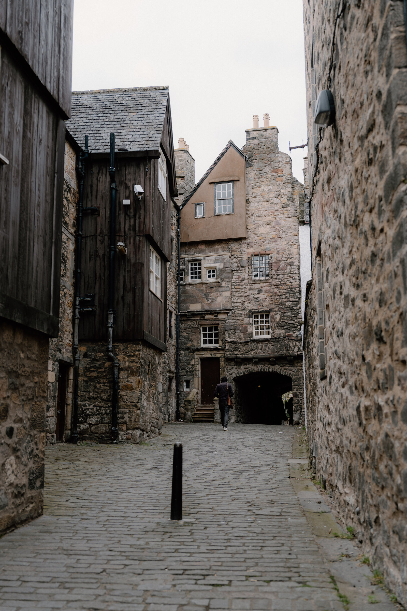A pedestrian walking through a cobbled Old Town courtyard in Edinburgh, timber and stone buildings framing the archway ahead.