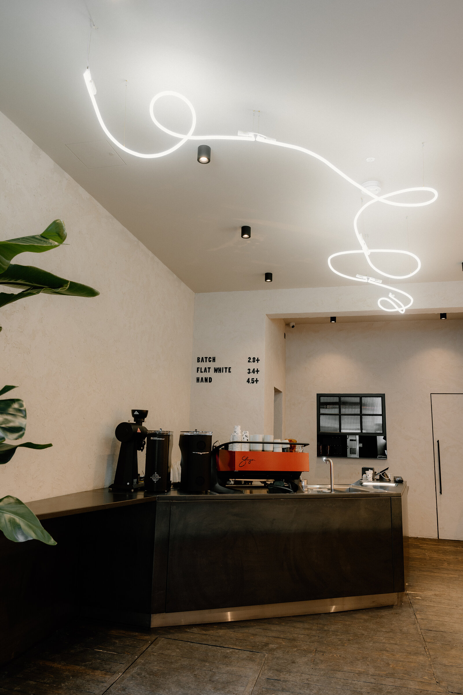 A looping neon light installation above a coffee counter in Edinburgh, a menu board listing batch, flat white and hand-brew prices.