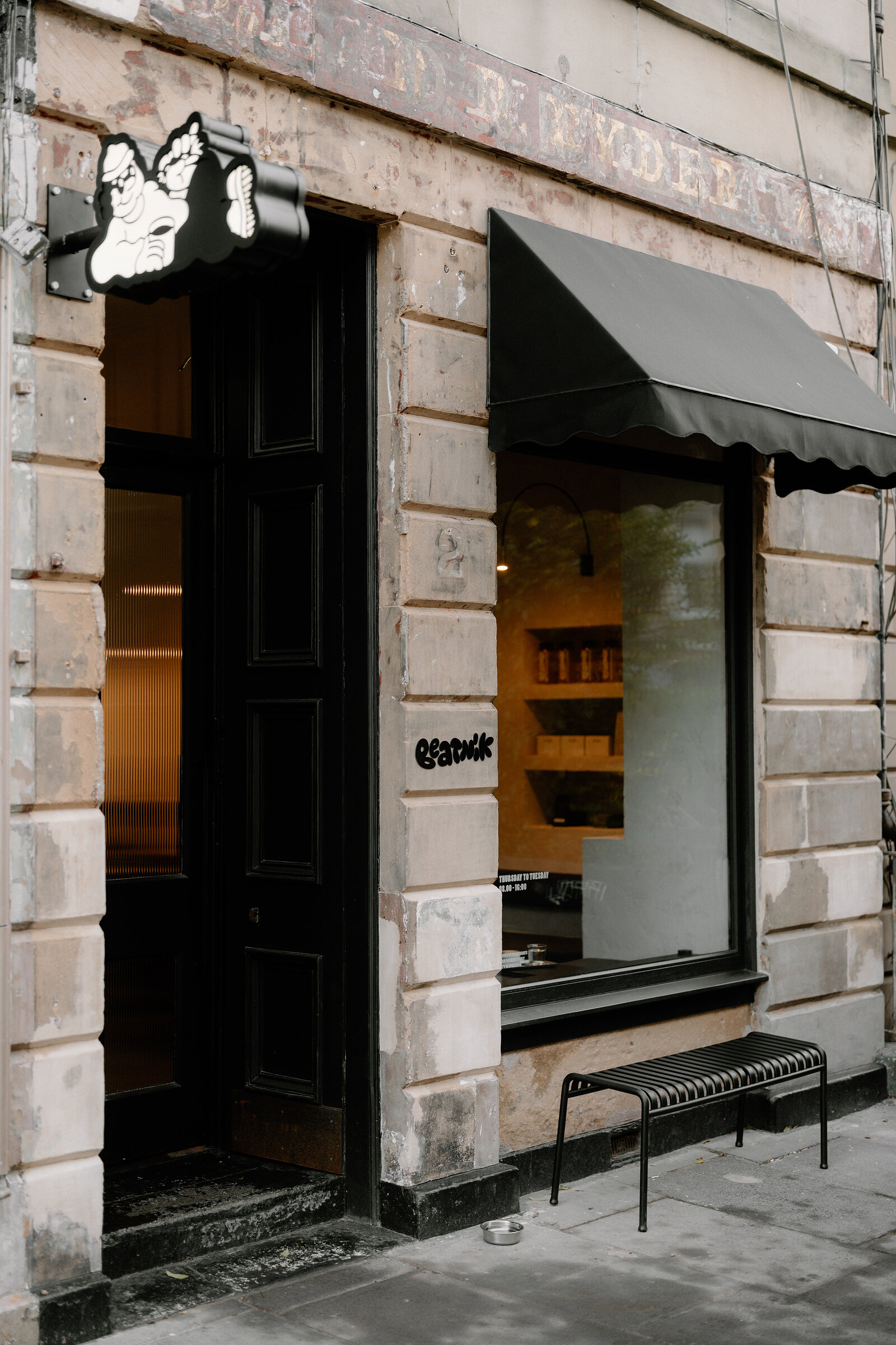 Beatnik's black doorway and illustrated sign sit beside a large window in a weathered sandstone building, a black awning shading the glass.