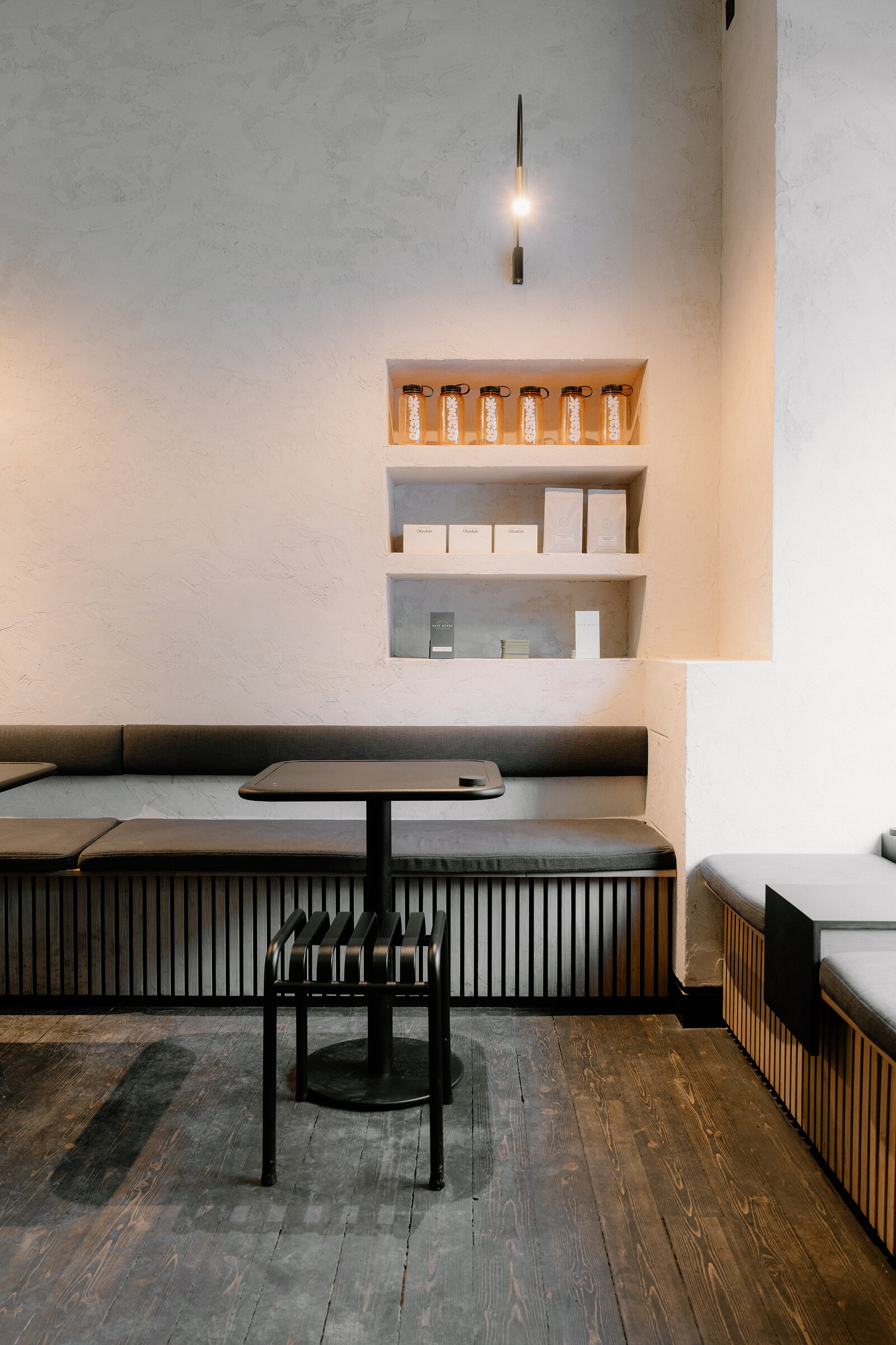 A minimalist dining nook in Edinburgh has a green banquette, a small round table and an alcove shelf stocked with bottled drinks.