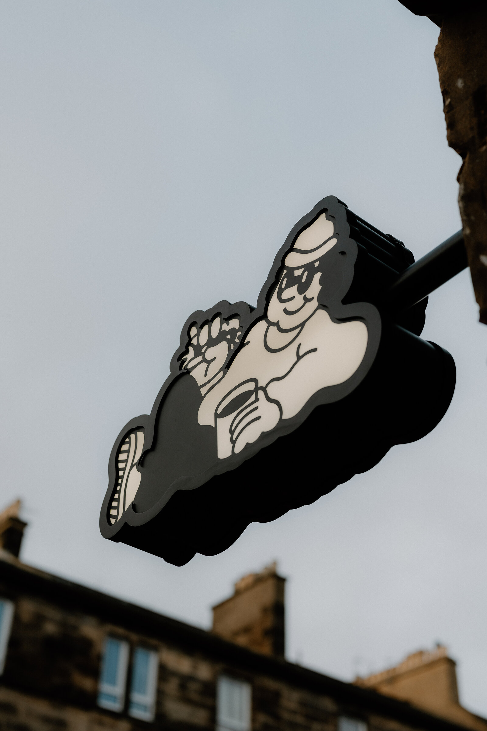 Beatnik's illustrated sign shows a reclining cartoon figure in sunglasses and a hat holding a cup, mounted above a shopfront with tenement rooftops behind.