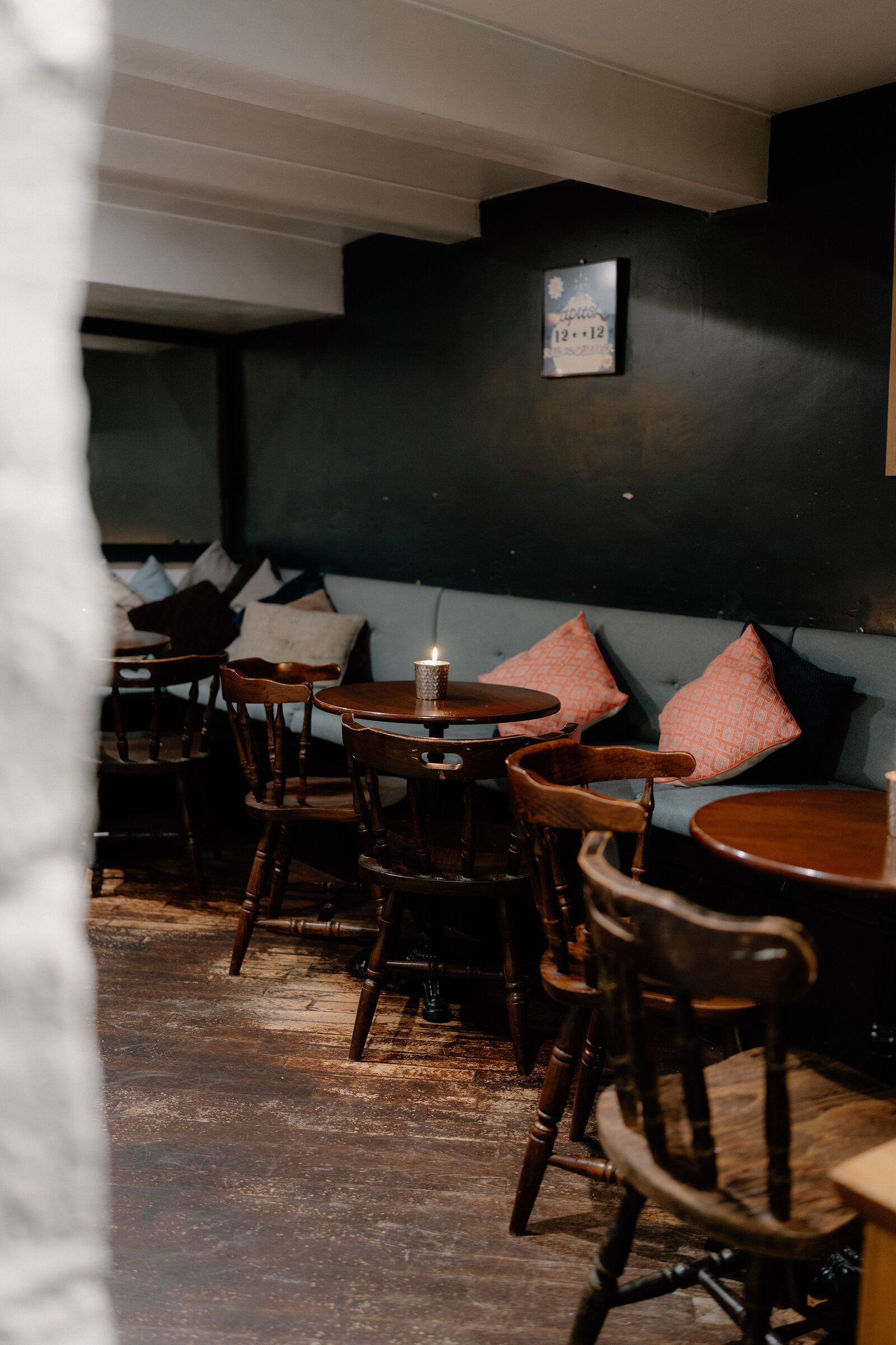 A cosy bar corner with a green banquette, pink cushions and small round tables lit by candlelight.