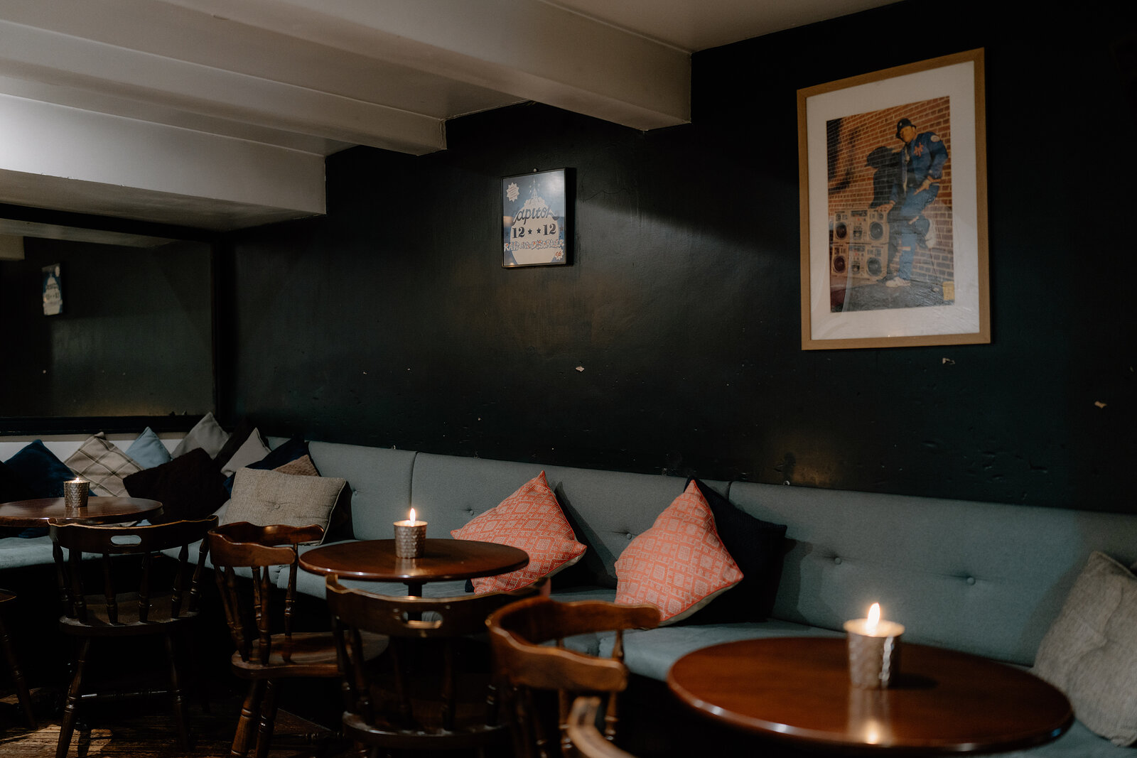 A dim bar interior with a green banquette, pink cushions and candlelit tables.