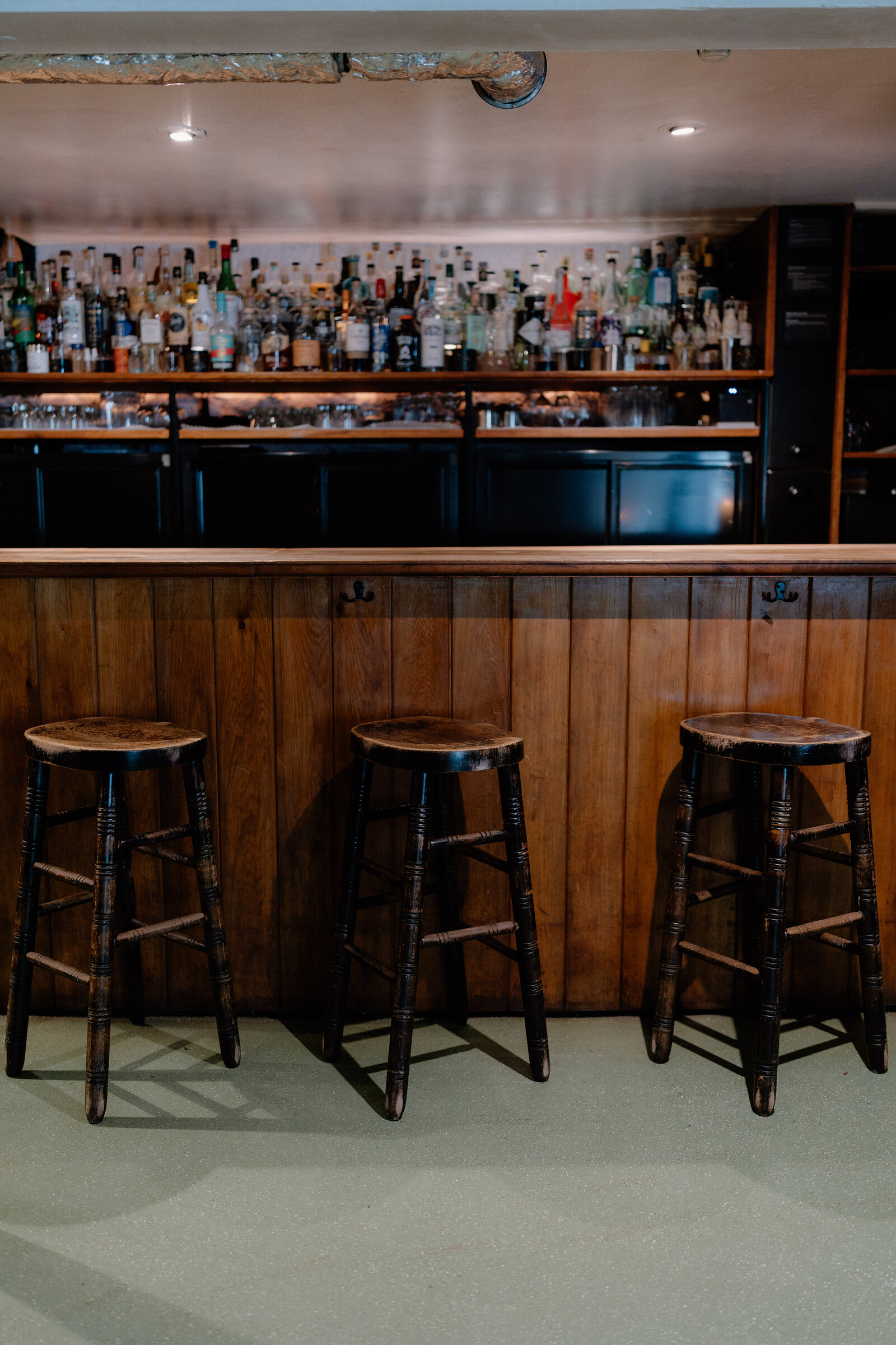 Empty wooden bar stools set before shelves of spirits in a dim Edinburgh bar.