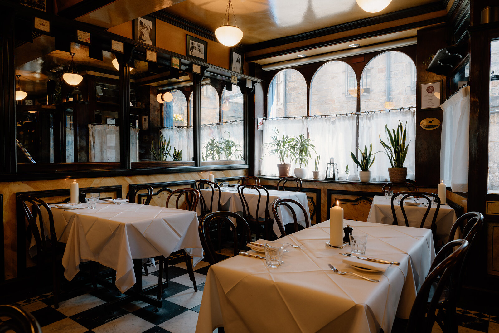 Arched windows and mirrored panels line a restaurant's black-and-white tiled dining room.