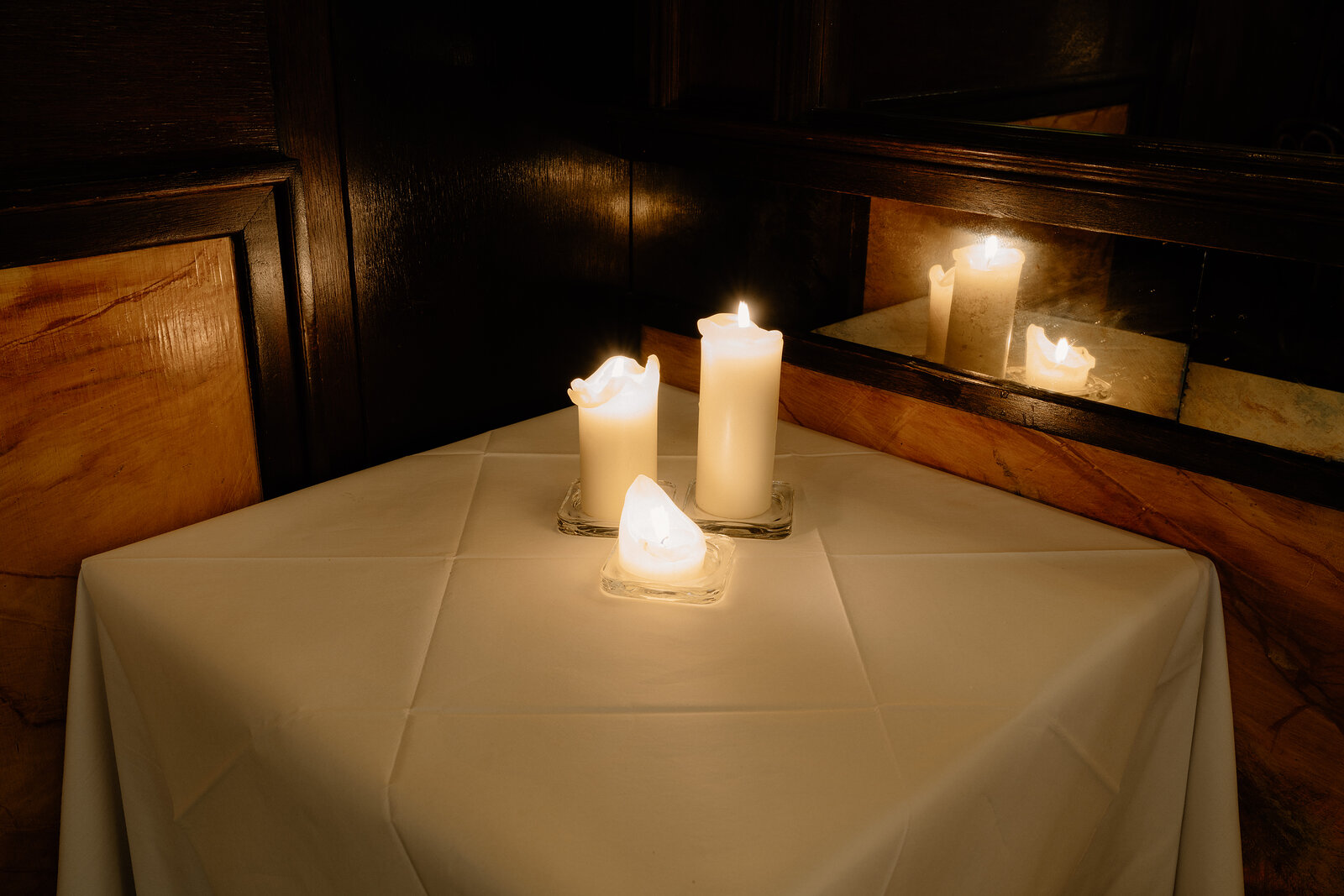Candles reflect in a mirror above a linen-covered table set in a dark-panelled restaurant corner.