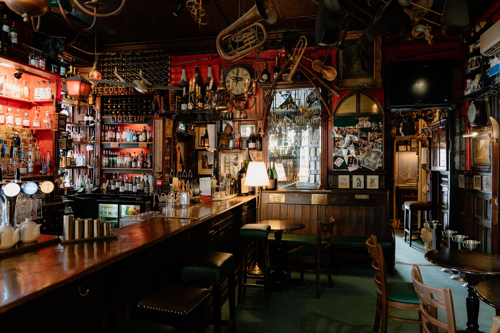 The Golden Drop's bar area shows green booth seating, a clock and rows of bottles beneath hanging brass instruments.