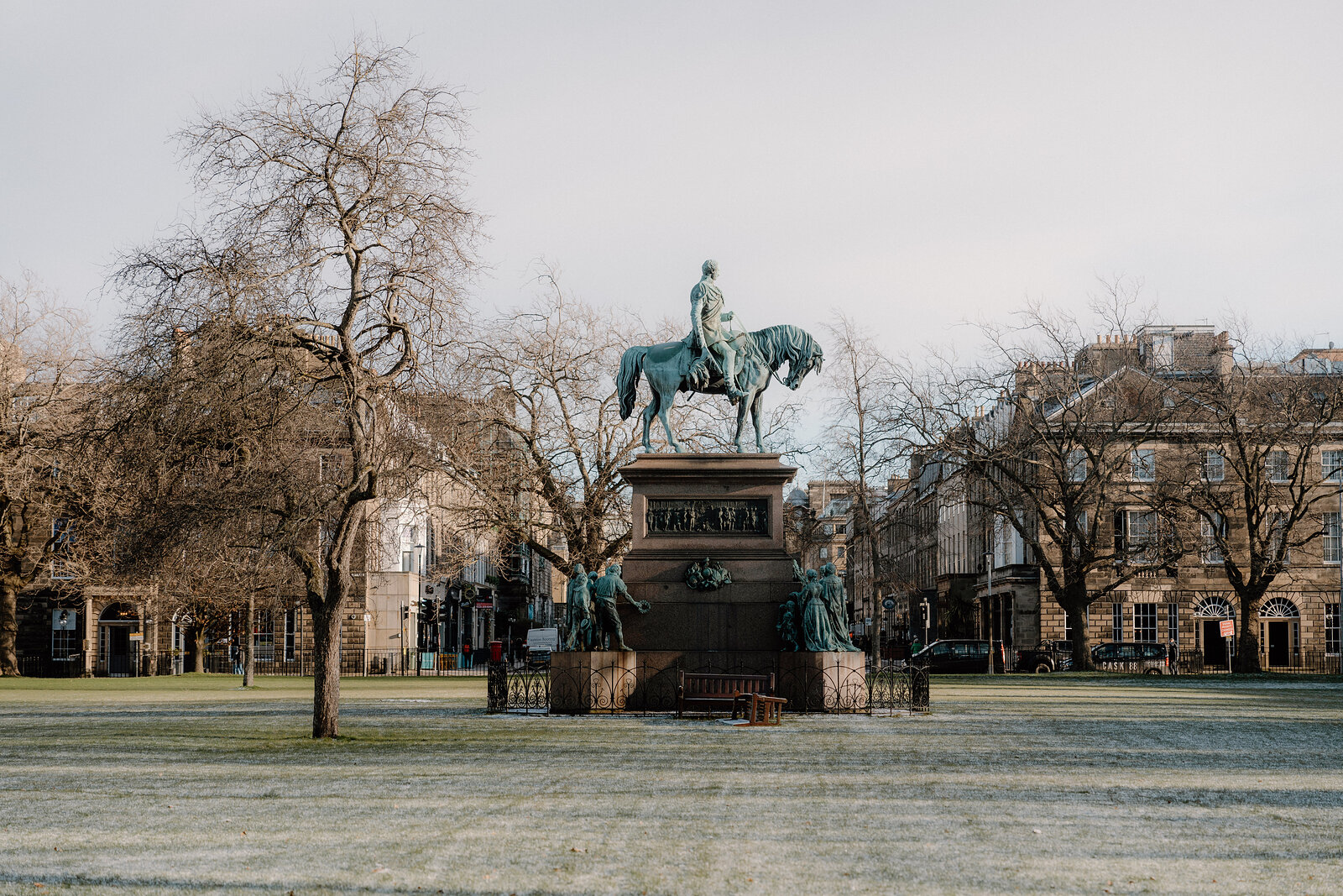 A bronze equestrian statue stands on a stone plinth in a frosted city square.
