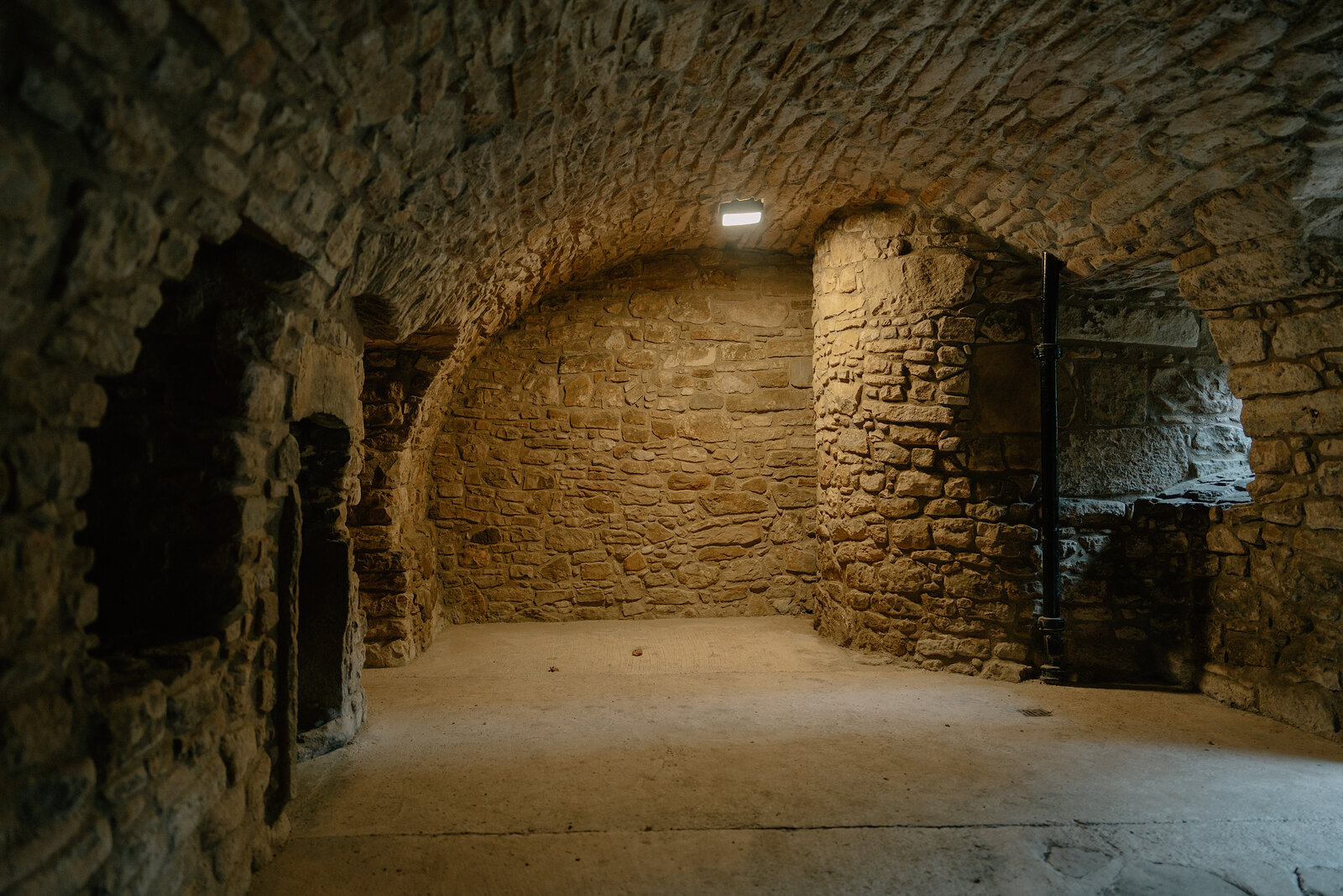 A stone-vaulted cellar curves into shadow beneath a low arched ceiling.
