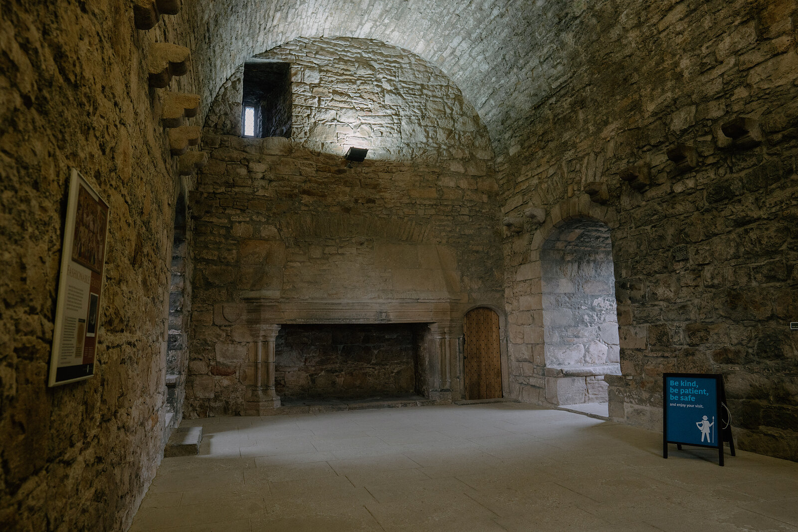 A stone-vaulted hall holds a fireplace flanked by an arched doorway and window.
