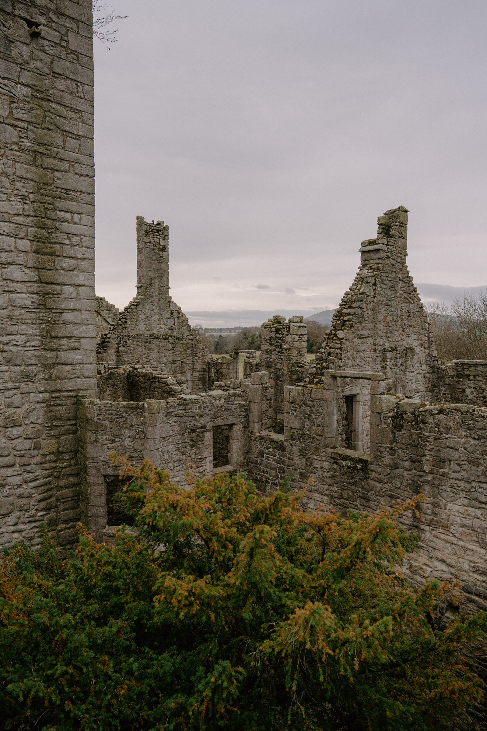 Autumn foliage grows before the crow-stepped gables of a ruined castle, hills rising beyond.