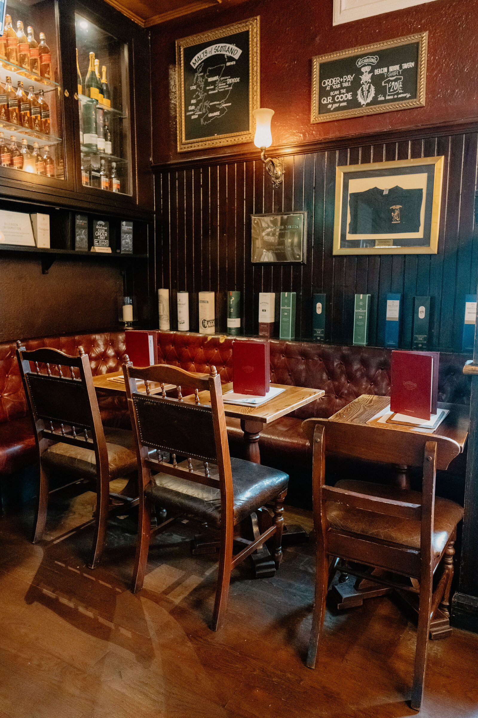 Leather chairs surround wooden tables beneath framed whisky maps and certificates.