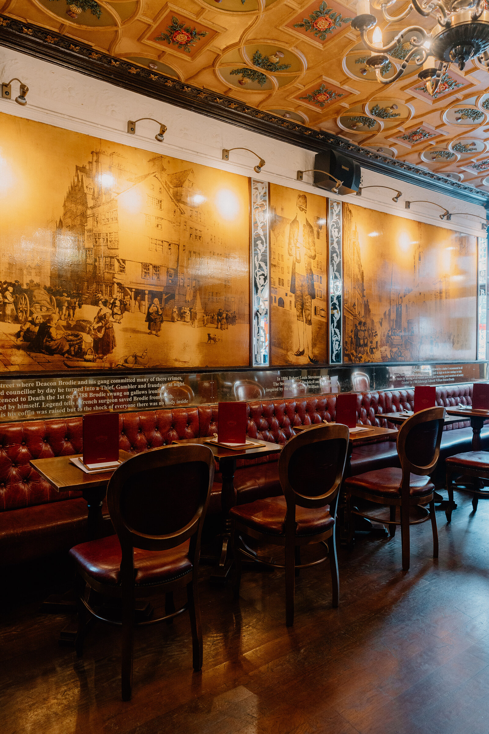 A mural of a historic street scene covers the wall above red leather booths at Deacon Brodie's Tavern.
