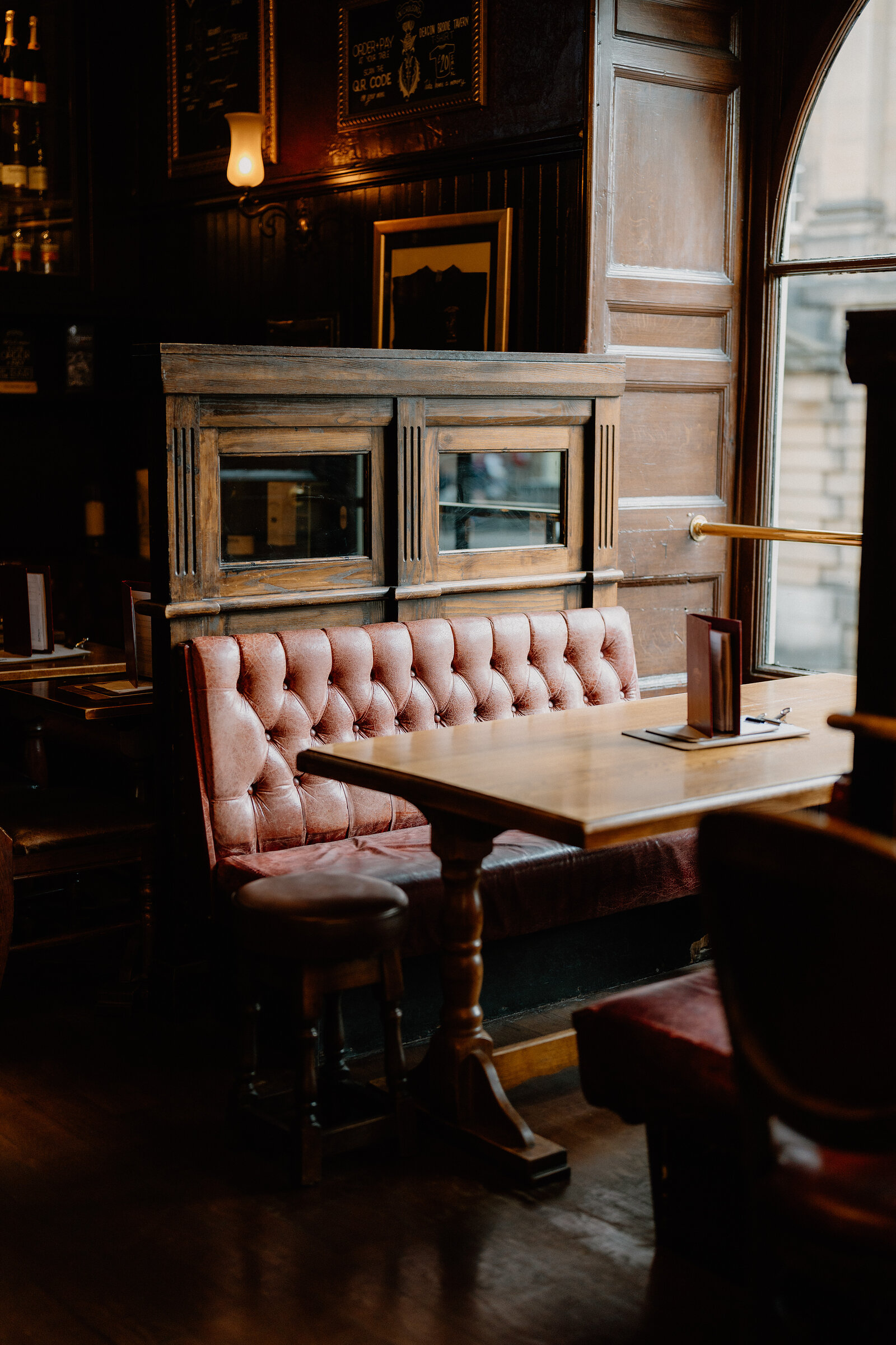 A mirrored wooden booth with leather benches sits beneath a wall clock in a pub.