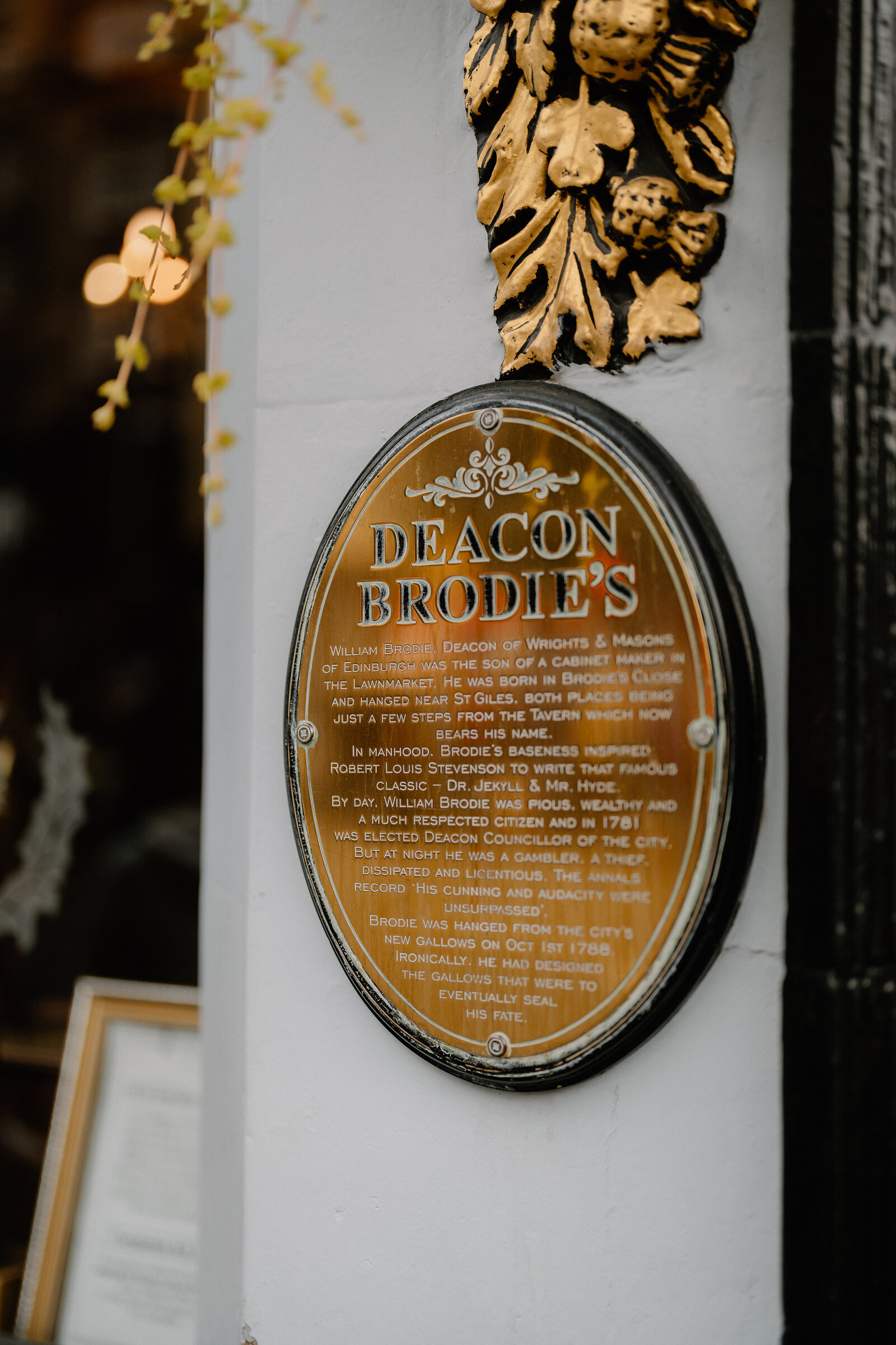 An ornate gold plaque recounts Deacon Brodie's life beneath carved foliage.