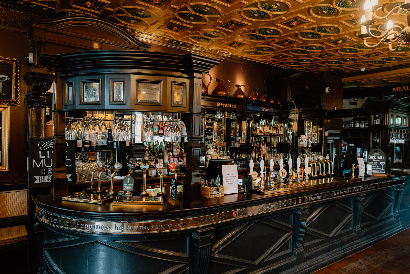 A long bar counter runs beneath an ornate painted ceiling in a pub.