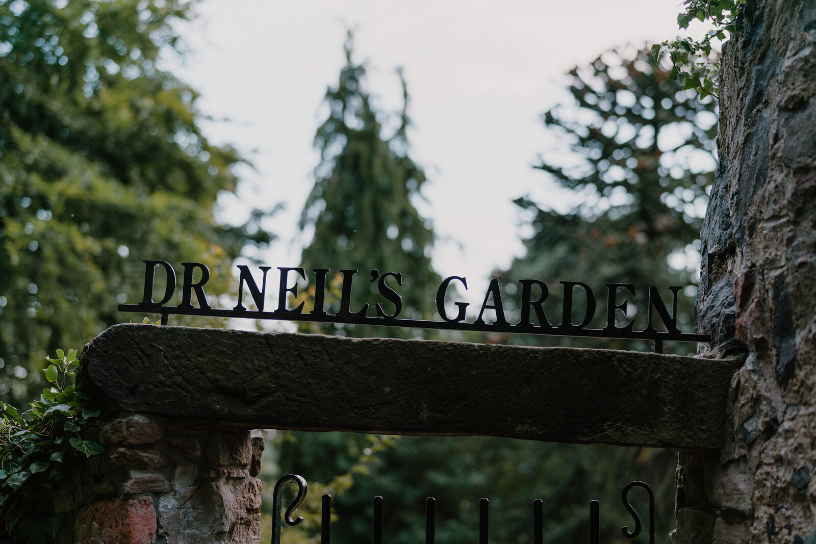 A sign reading "Dr Neil's Garden" is mounted on an iron gate arch.