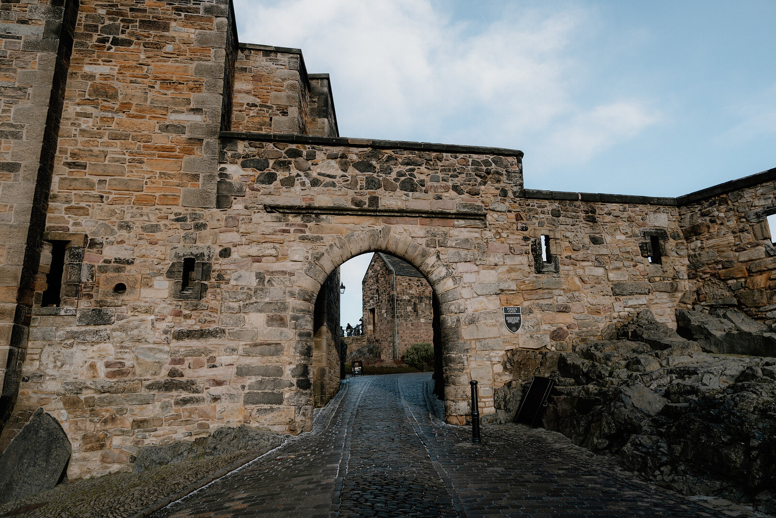 A stone gatehouse arch at Edinburgh Castle opens onto a cobbled road beneath the castle walls.