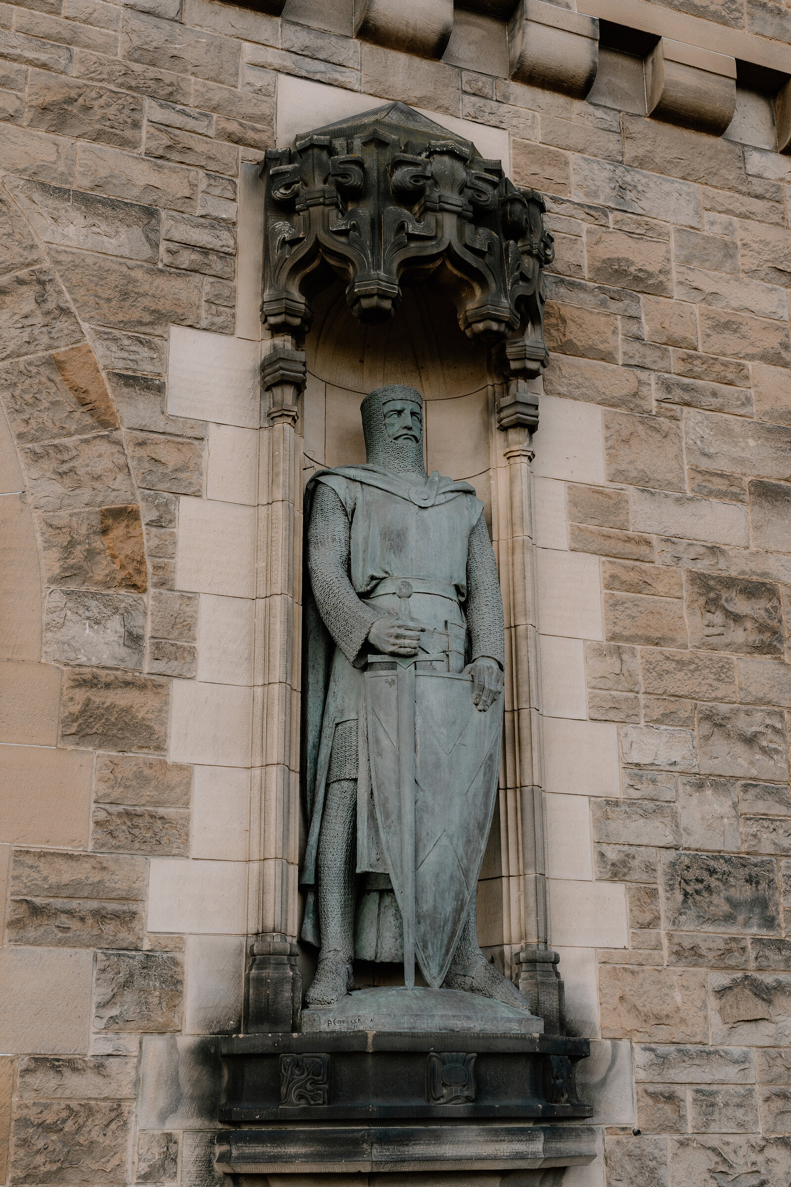 A bronze statue of an armoured knight stands in a carved stone niche on Edinburgh Castle's wall.