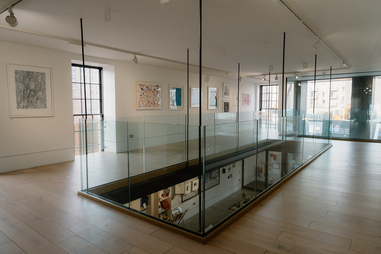 A glass-floored gallery mezzanine overlooks framed prints displayed on the level below.