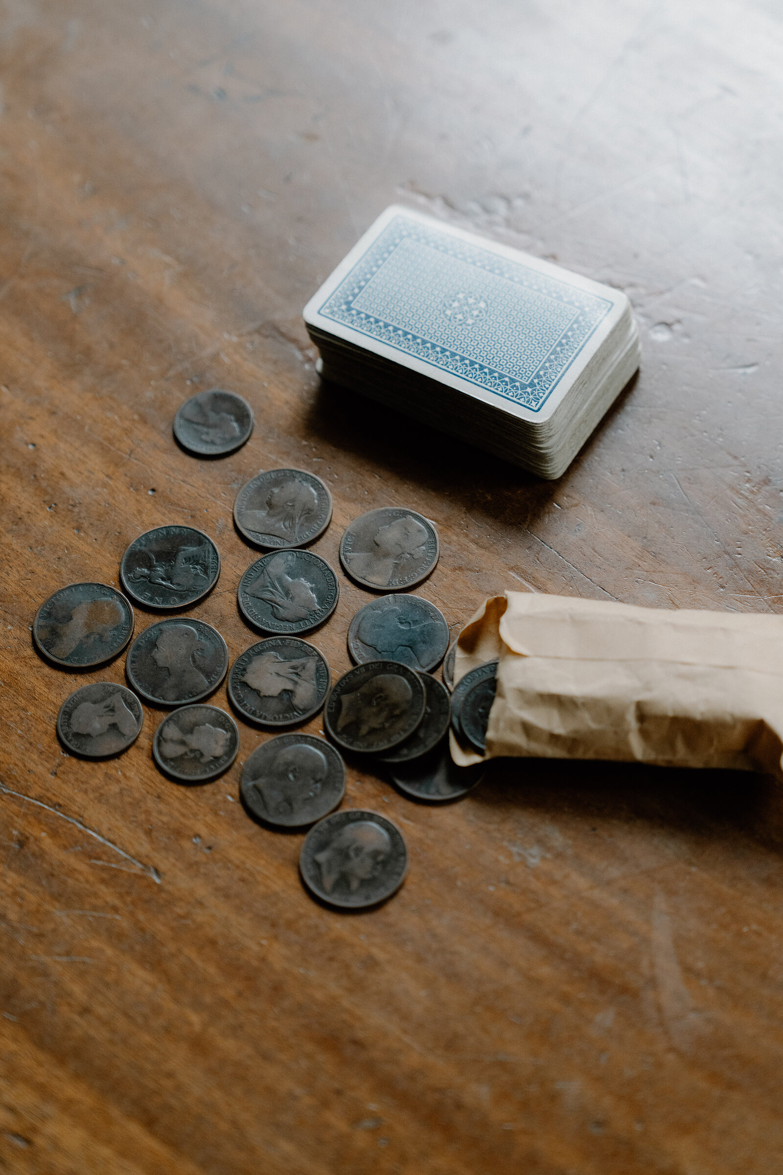 Antique coins and a pack of playing cards spill from a paper bag onto a wooden table.