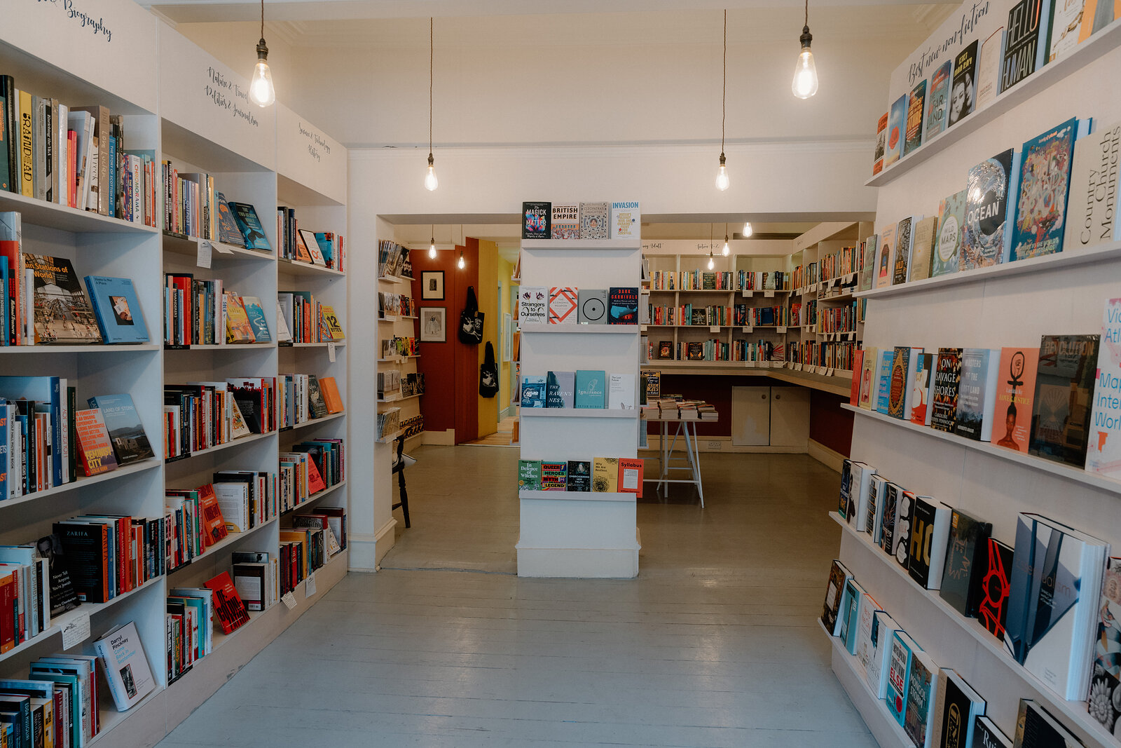 Aisles of books line painted shelving beneath hanging bulb lights at Golden Hare Books.