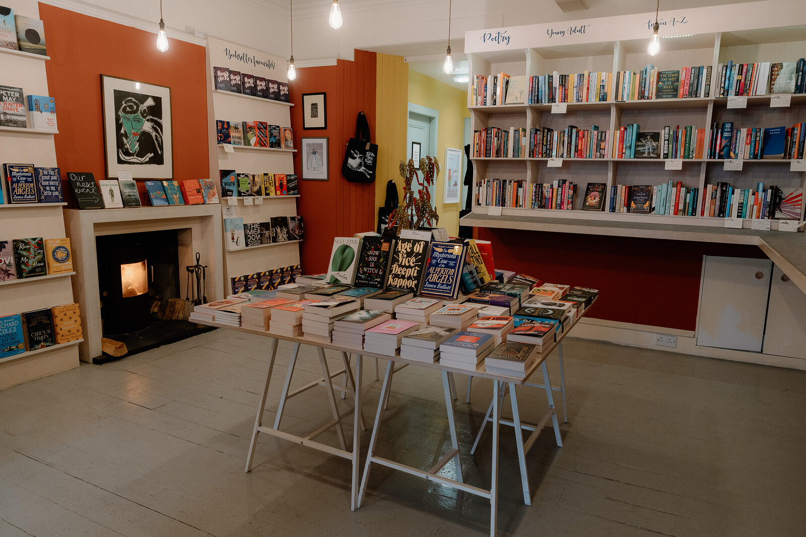 Books are laid out on a trestle table beneath tall shelving at Golden Hare Books, a lit fireplace in the corner.