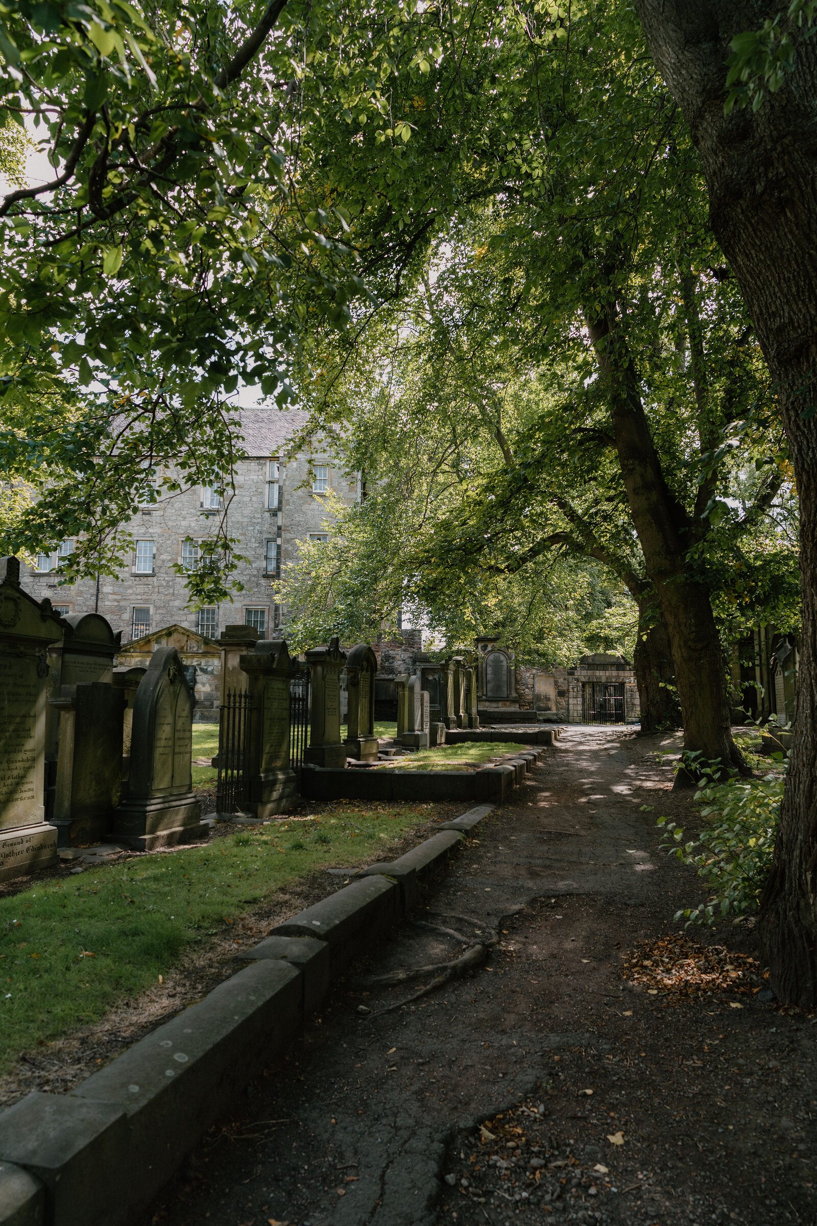 A shaded path winds between old gravestones and tall trees at Greyfriars Kirkyard.