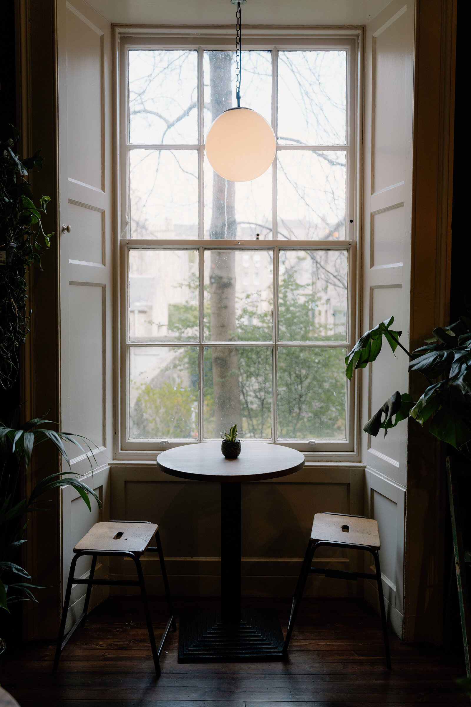 A small round table and stools sit in a window nook surrounded by potted plants at grow urban.
