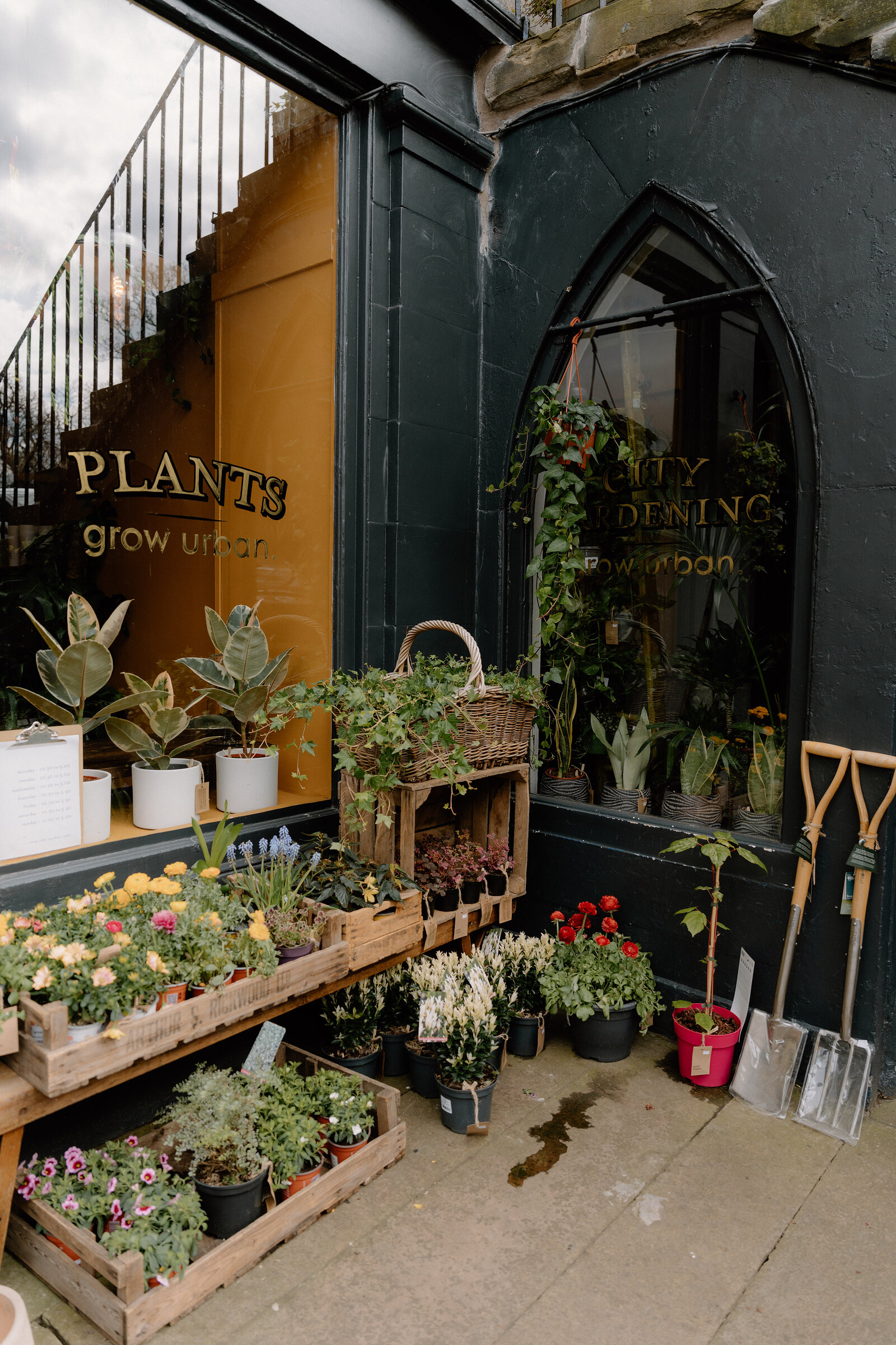 Garden tools and potted flowers line the arched doorway of grow urban's shopfront.