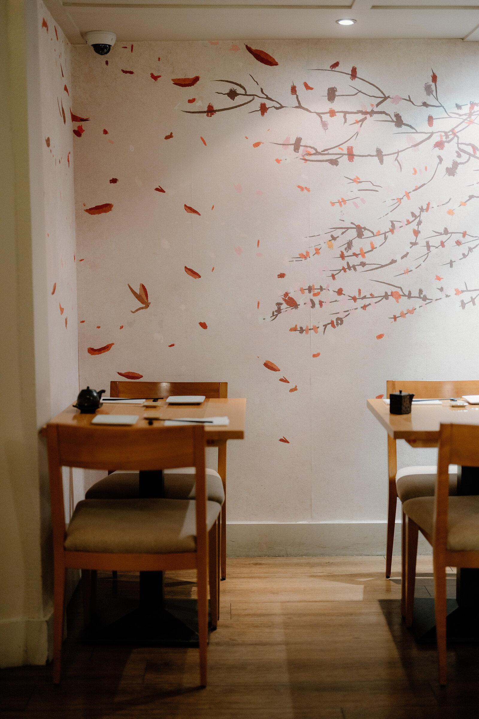 A cherry-blossom branch mural with scattered petals covers the wall above two tables in a Japanese restaurant.