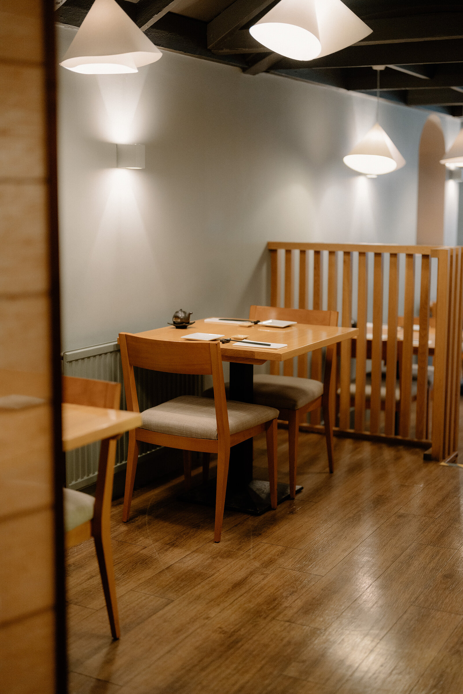 A table set with a small teapot stands beside a wooden slatted partition in a softly lit Japanese restaurant.