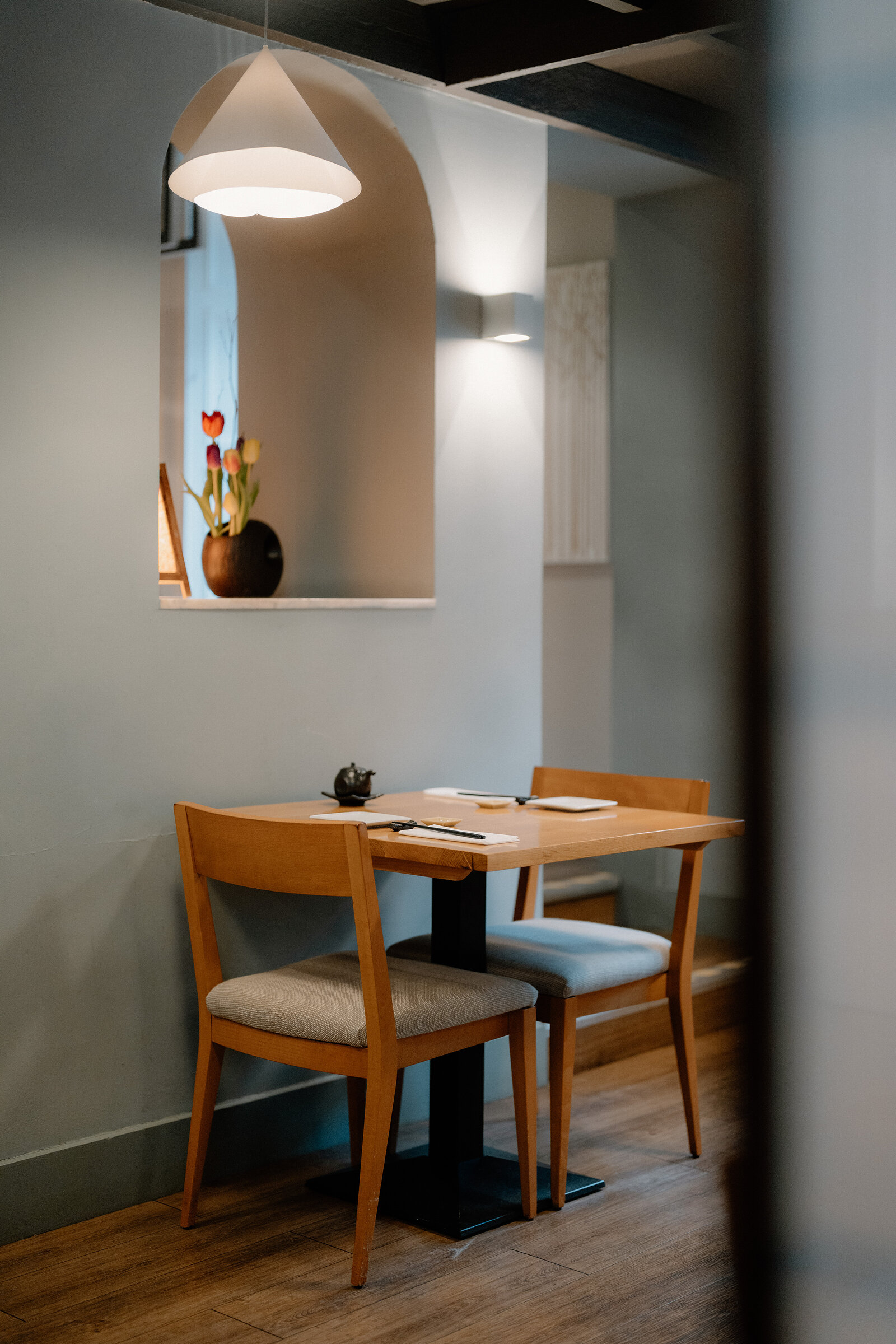 A small table with tulips in an alcove sits beneath an arched doorway and pendant light in a restaurant.