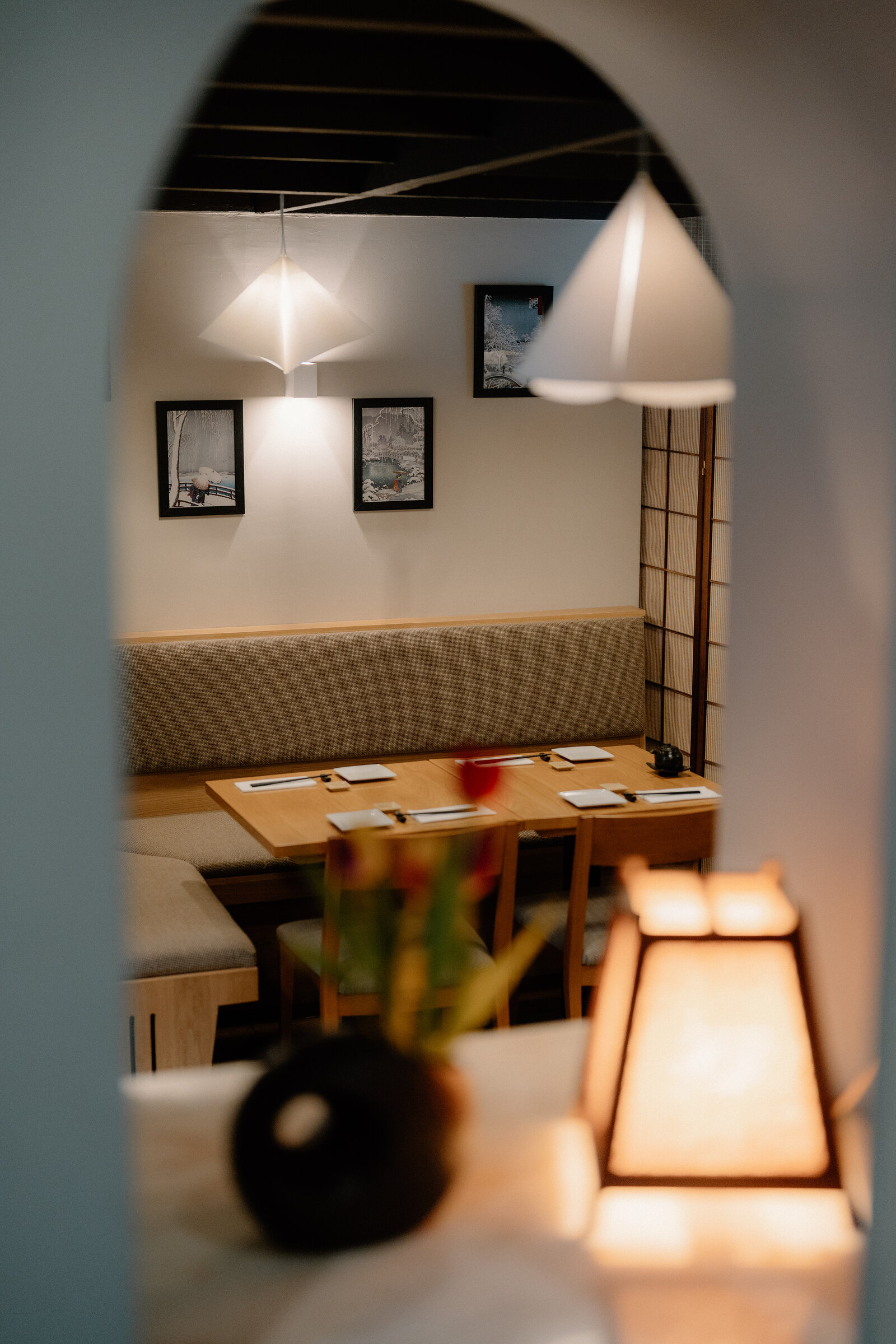 An arched doorway frames a booth table set with chopsticks beneath triangular pendant lights in a Japanese restaurant.