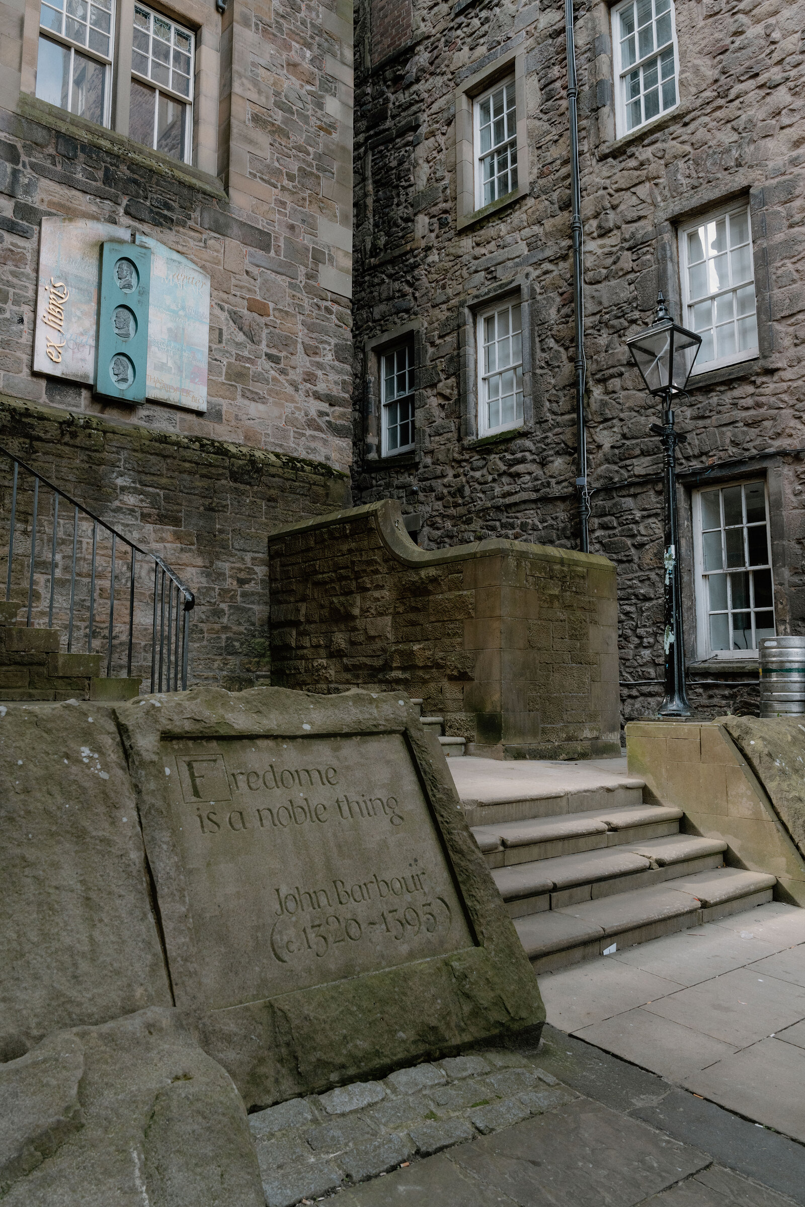 A carved stone slab quoting John Barbour, 'Fredome is a noble thing', lies in a paved courtyard beside a stone stairway.