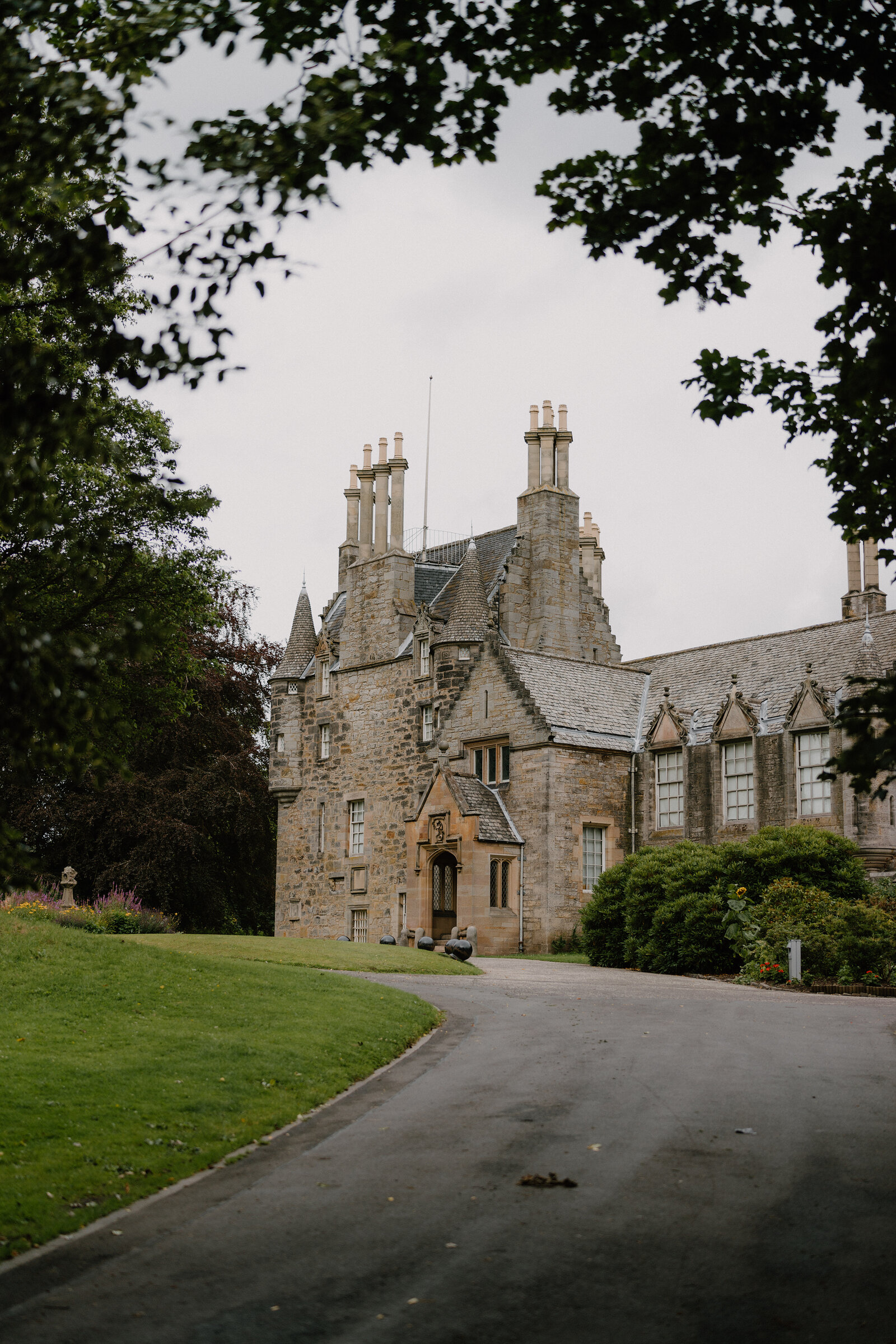 Lauriston Castle's turreted stone facade rises behind trees at the end of a curving driveway.