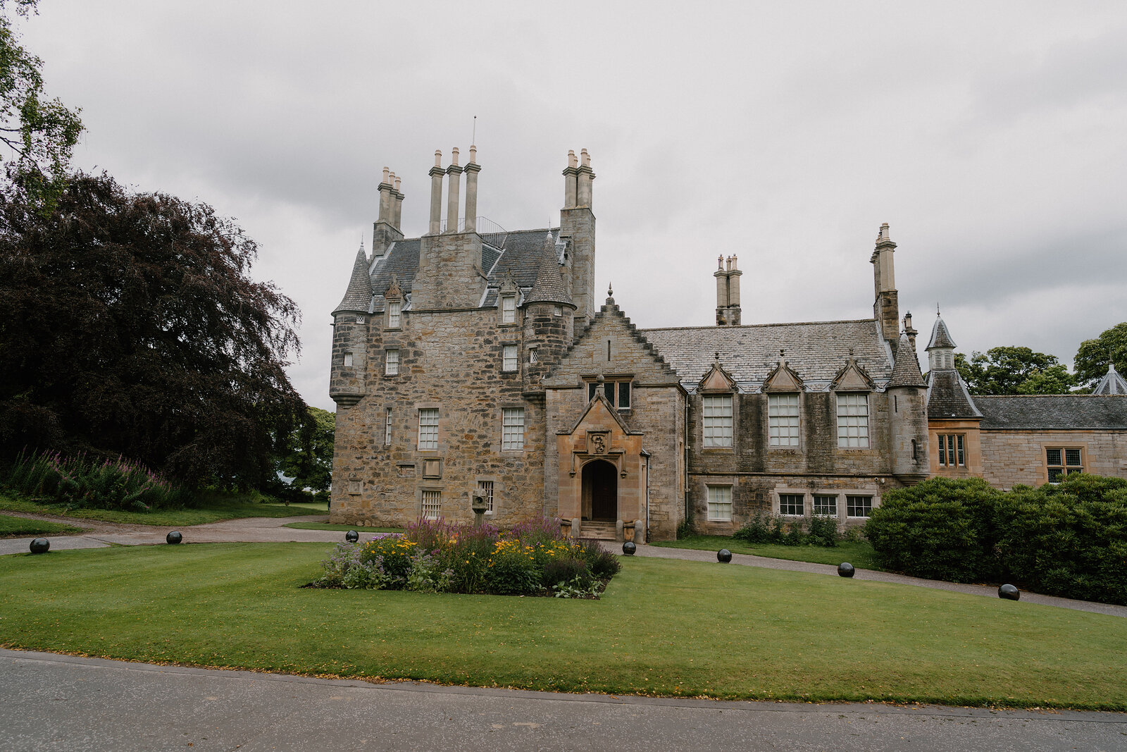 Lauriston Castle's turreted stone entrance overlooks a lawn bordered by flower beds and clipped hedges.