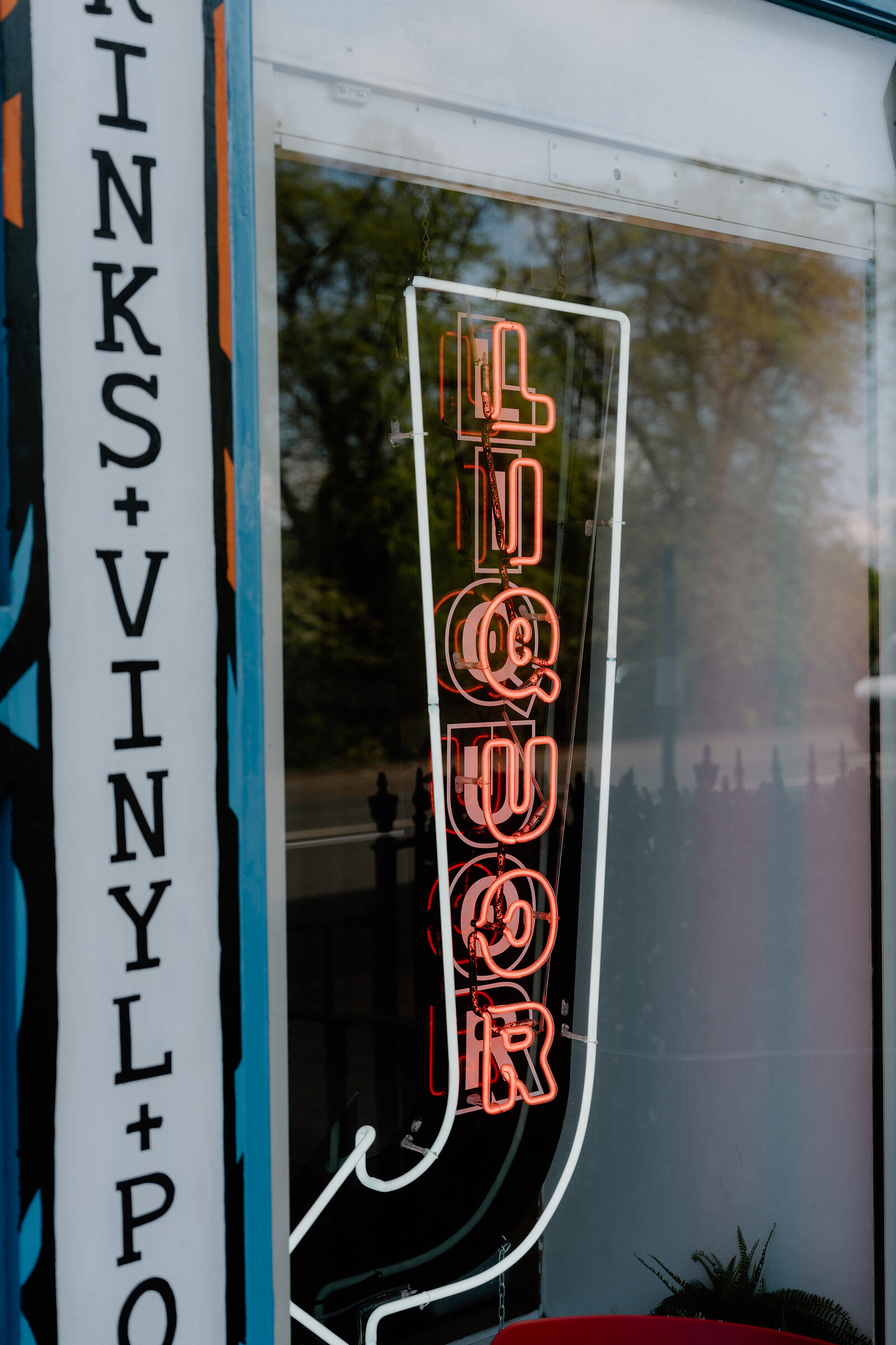 A neon Liquor sign glows behind a window advertising drinks and vinyl in Edinburgh.