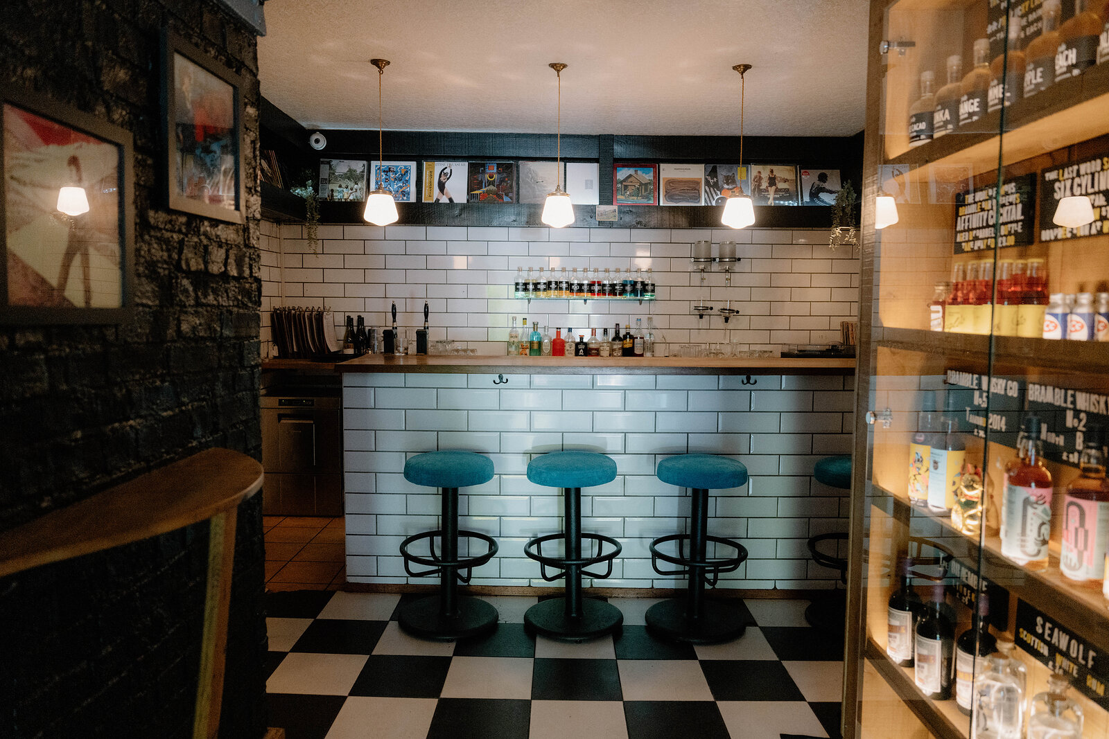 Teal velvet stools line a subway-tiled bar beneath shelves of vinyl records in Edinburgh.