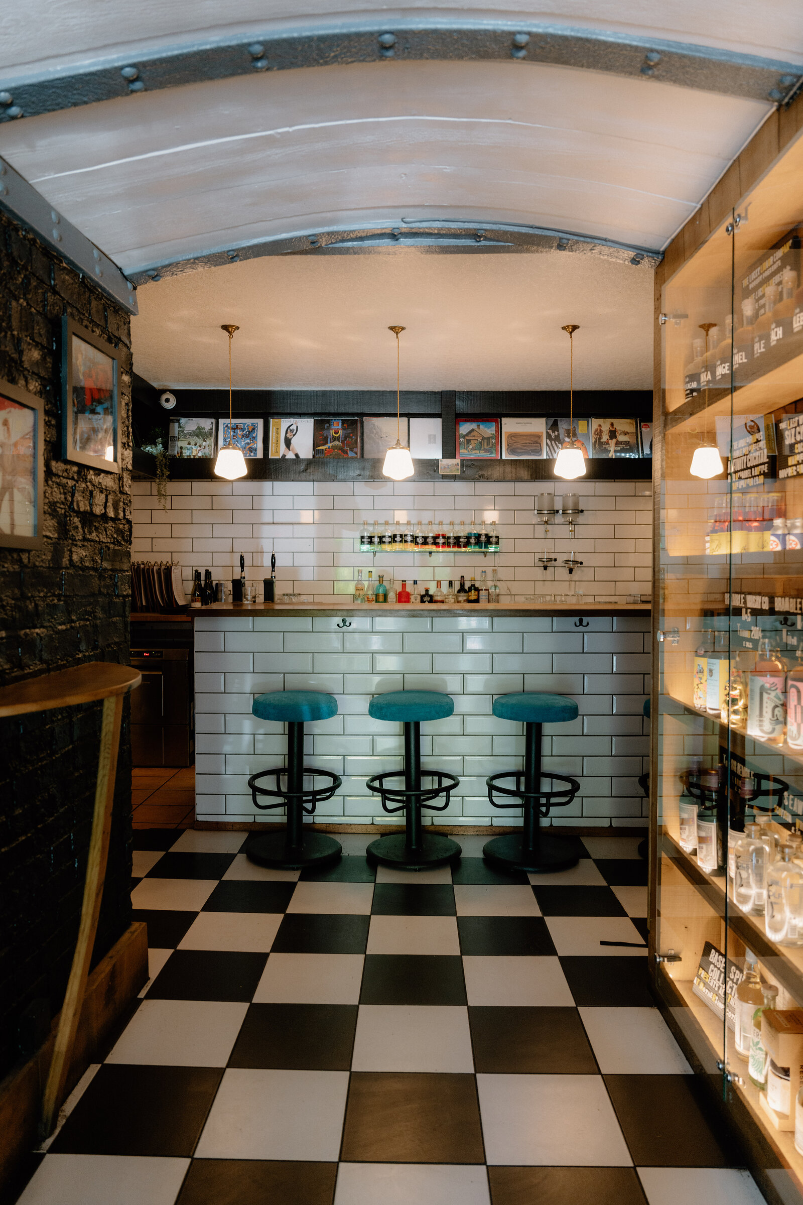 A subway-tiled bar with teal stools sits beneath a curved ceiling and shelves of framed record sleeves in Edinburgh.